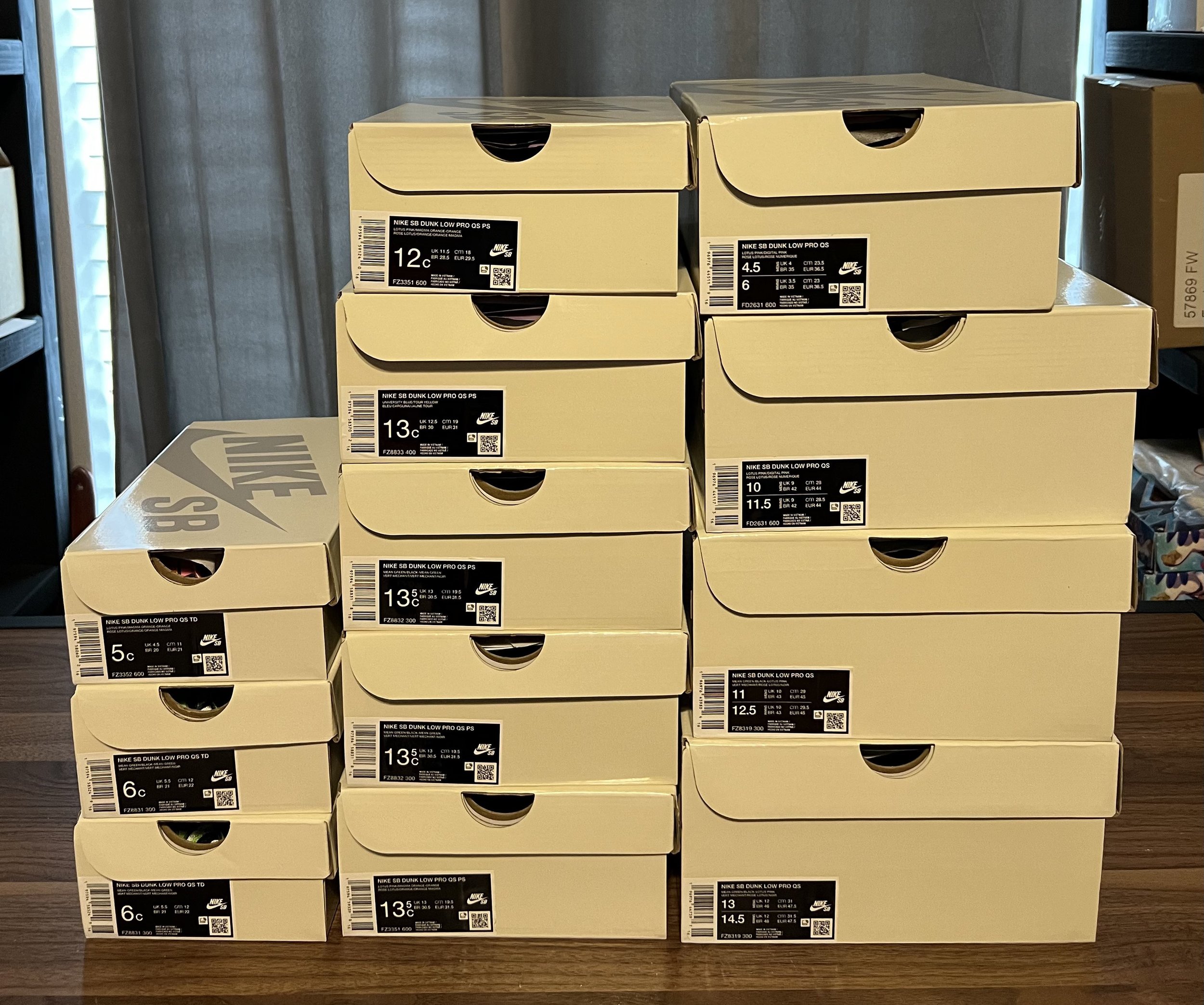 Stack of Nike shoe boxes on a wooden surface in front of a gray wall and window, with sizes labeled on each box.