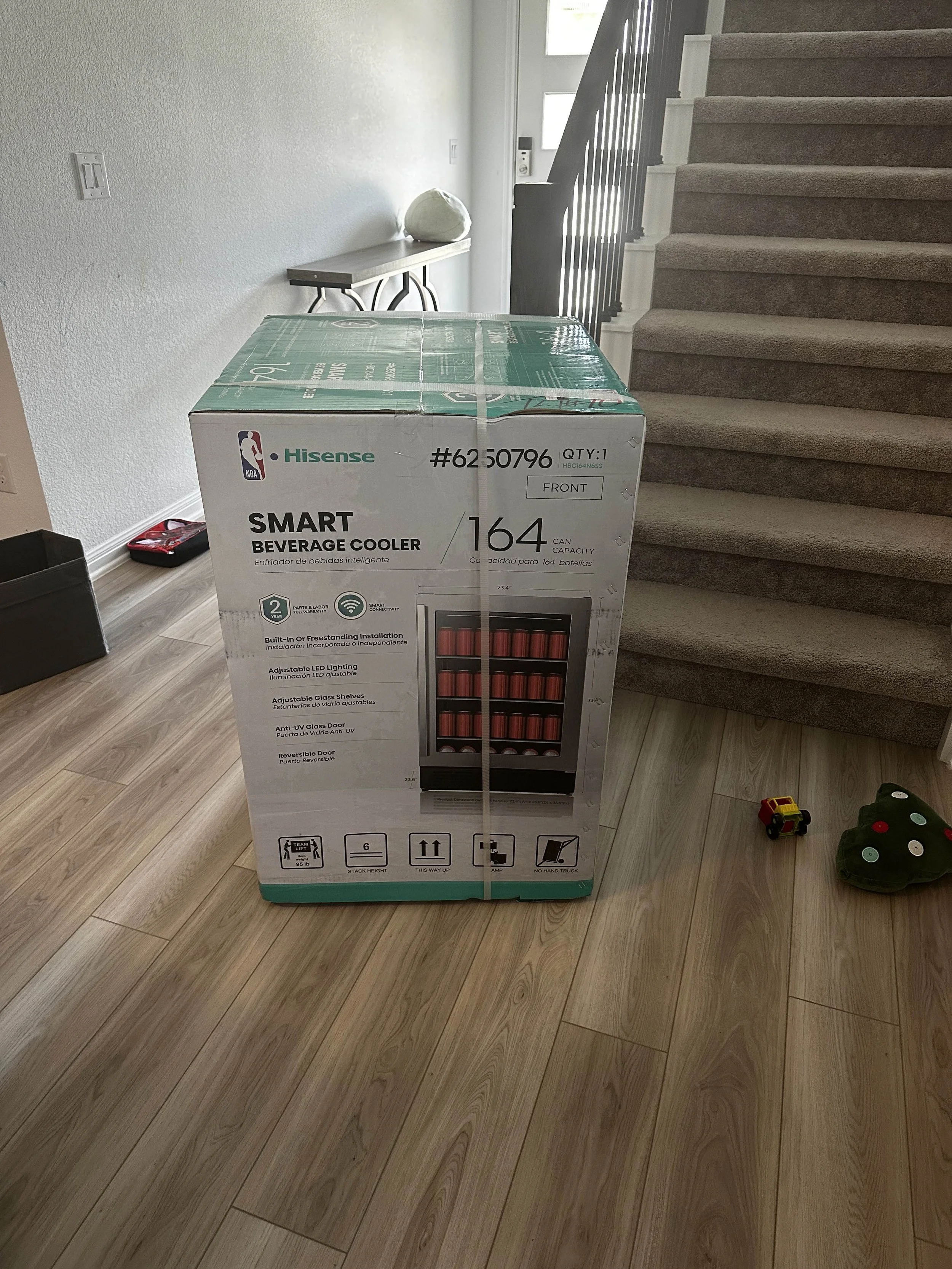 Boxed Hisense smart beverage cooler on a wooden floor near a staircase with carpeted steps.