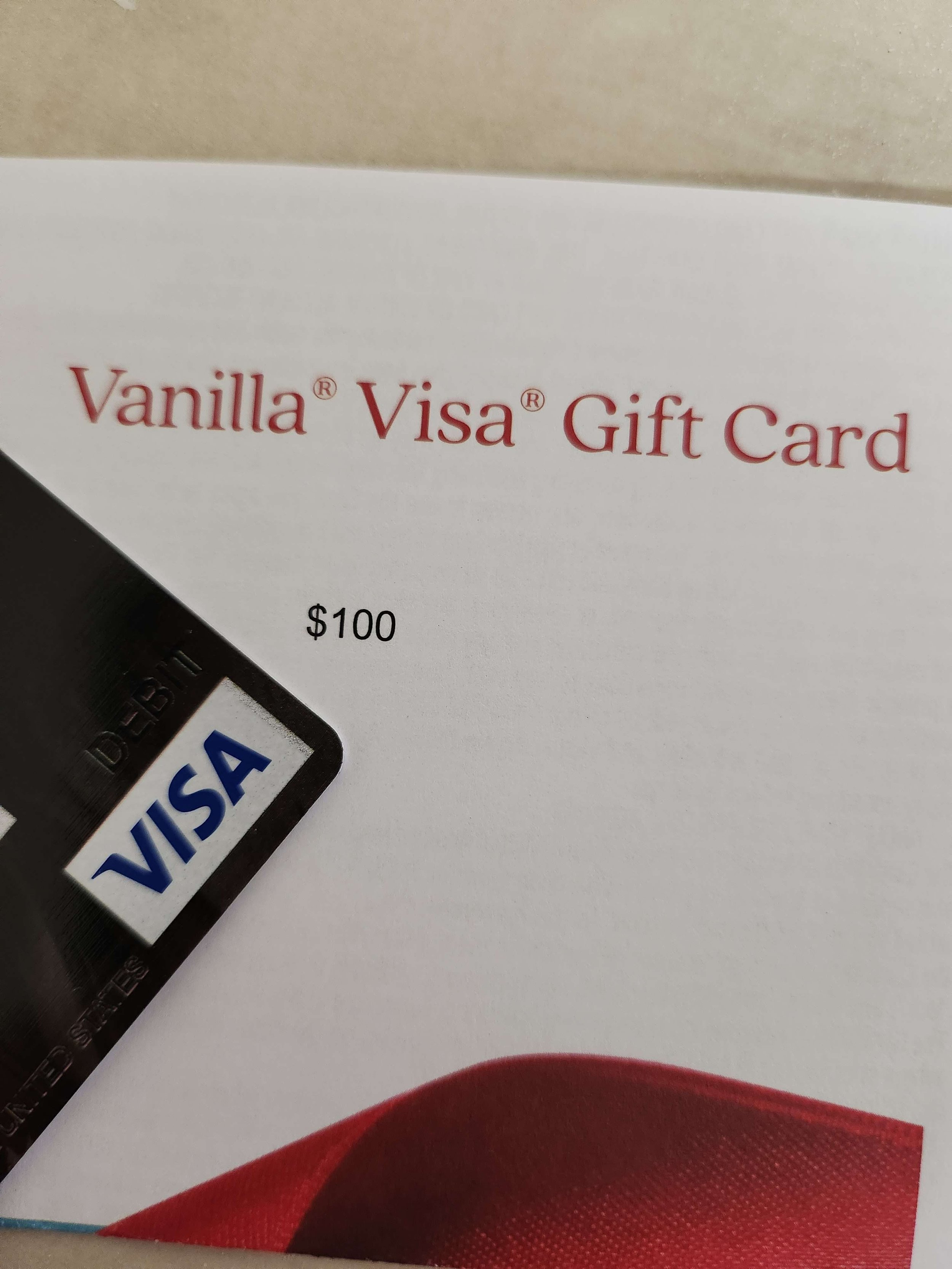A Vanilla Visa gift card with a $100 value, partially visible, placed on top of a white background with a red design.
