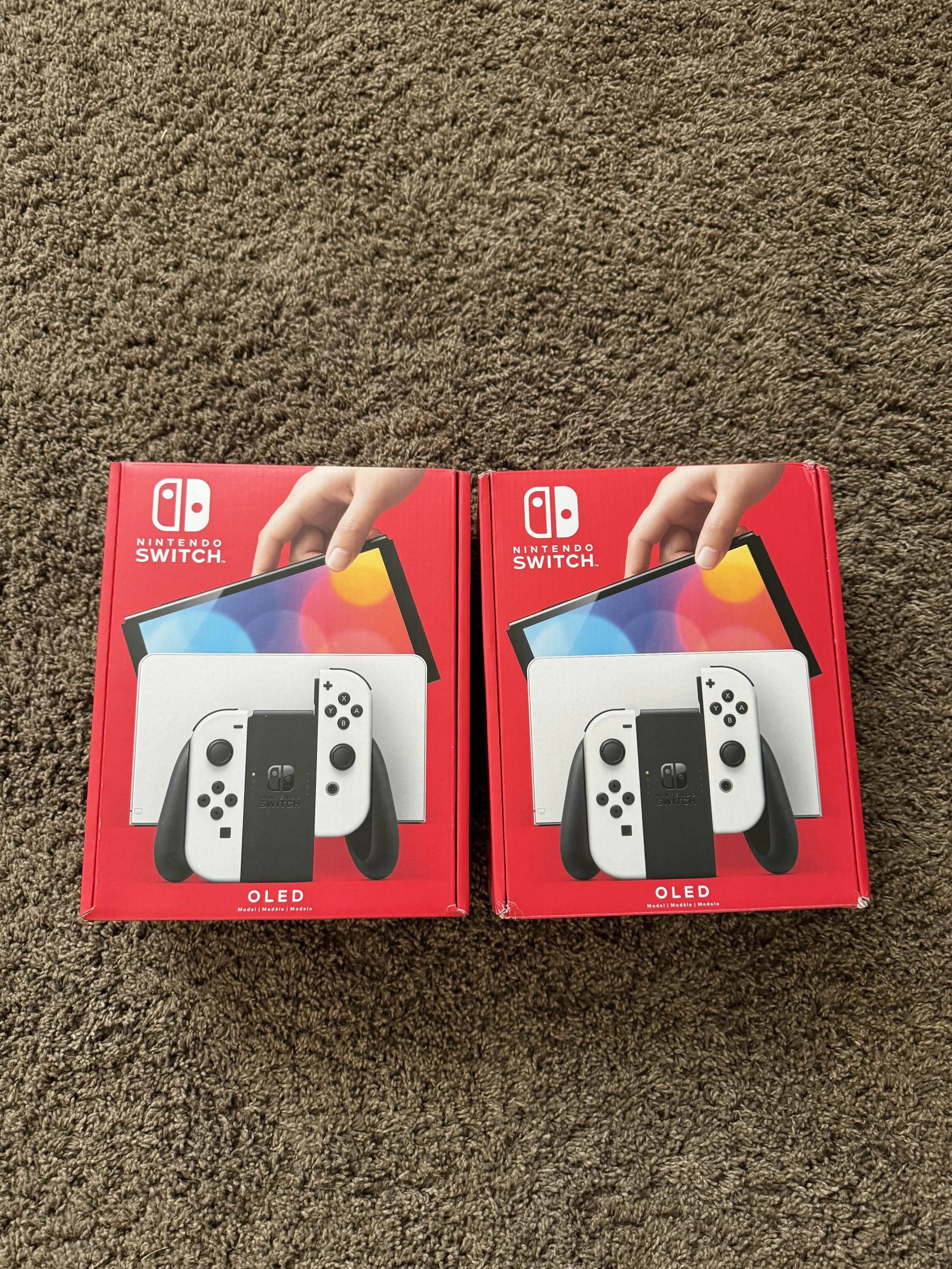 Two Nintendo Switch OLED console boxes on a brown carpet.