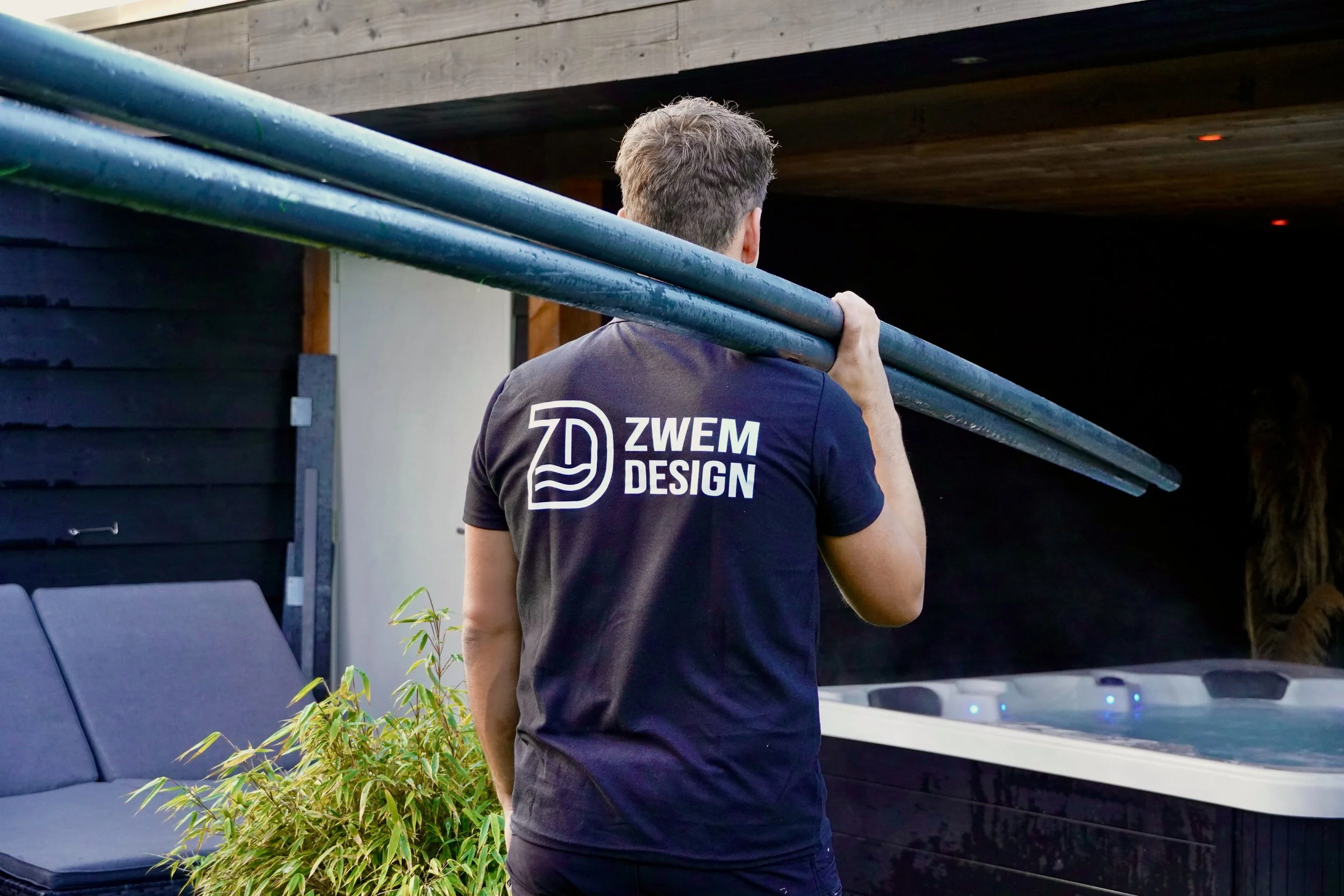 Man met zwemmer's shirt die lange buis in schouder draagt, naast jacuzzi buiten.