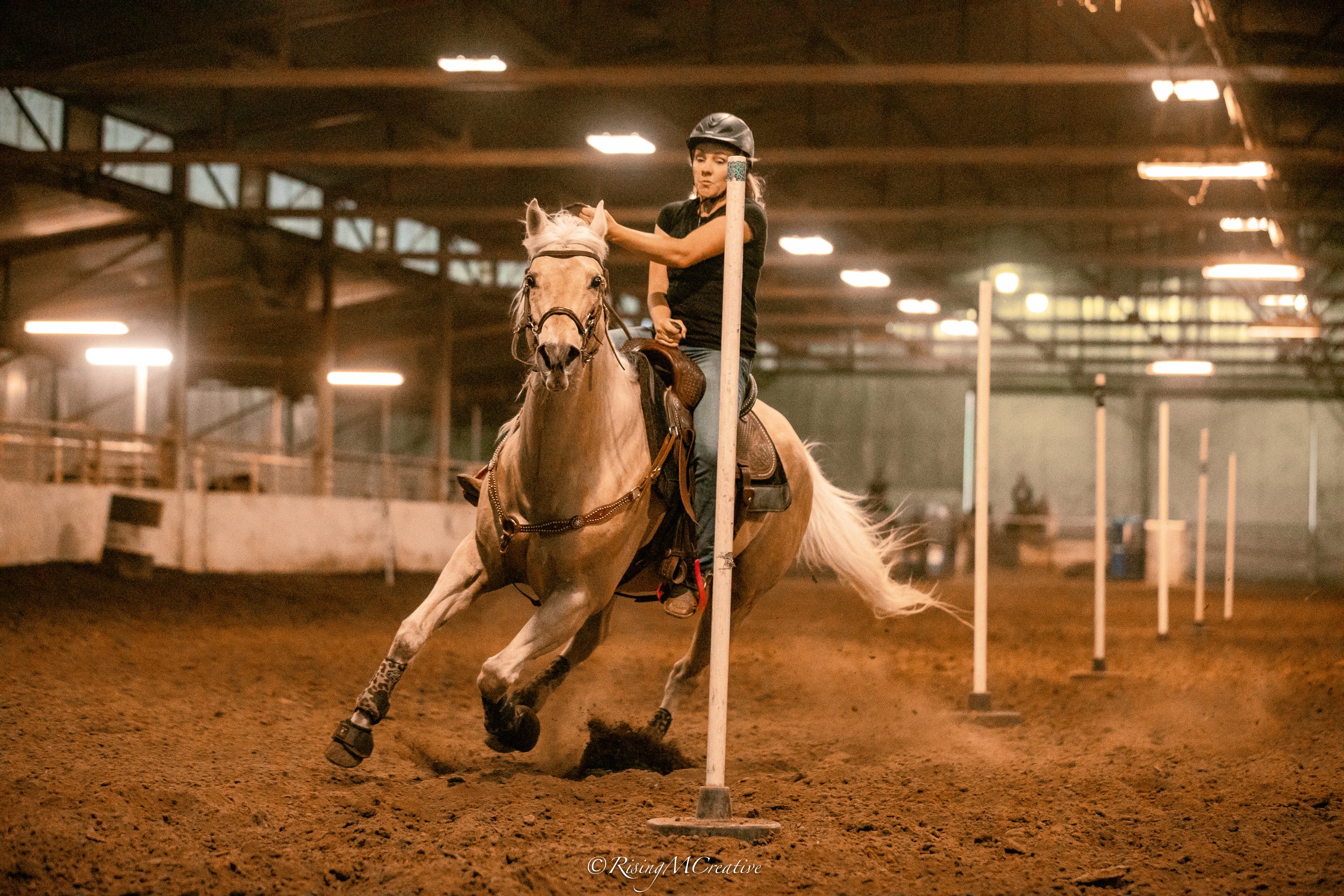 A woman riding a bucking horse in a rodeo arena, pursuing a calf.