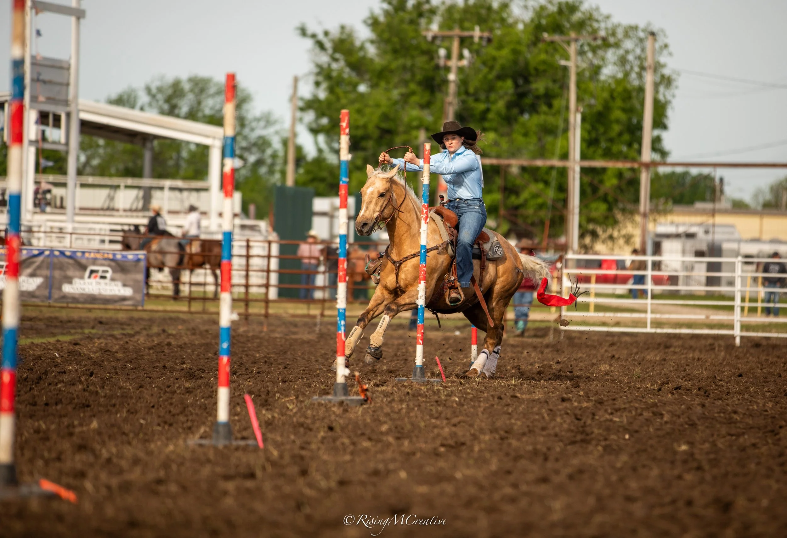 A woman riding a horse through a show jumping course with colorful poles in an outdoor arena during daytime