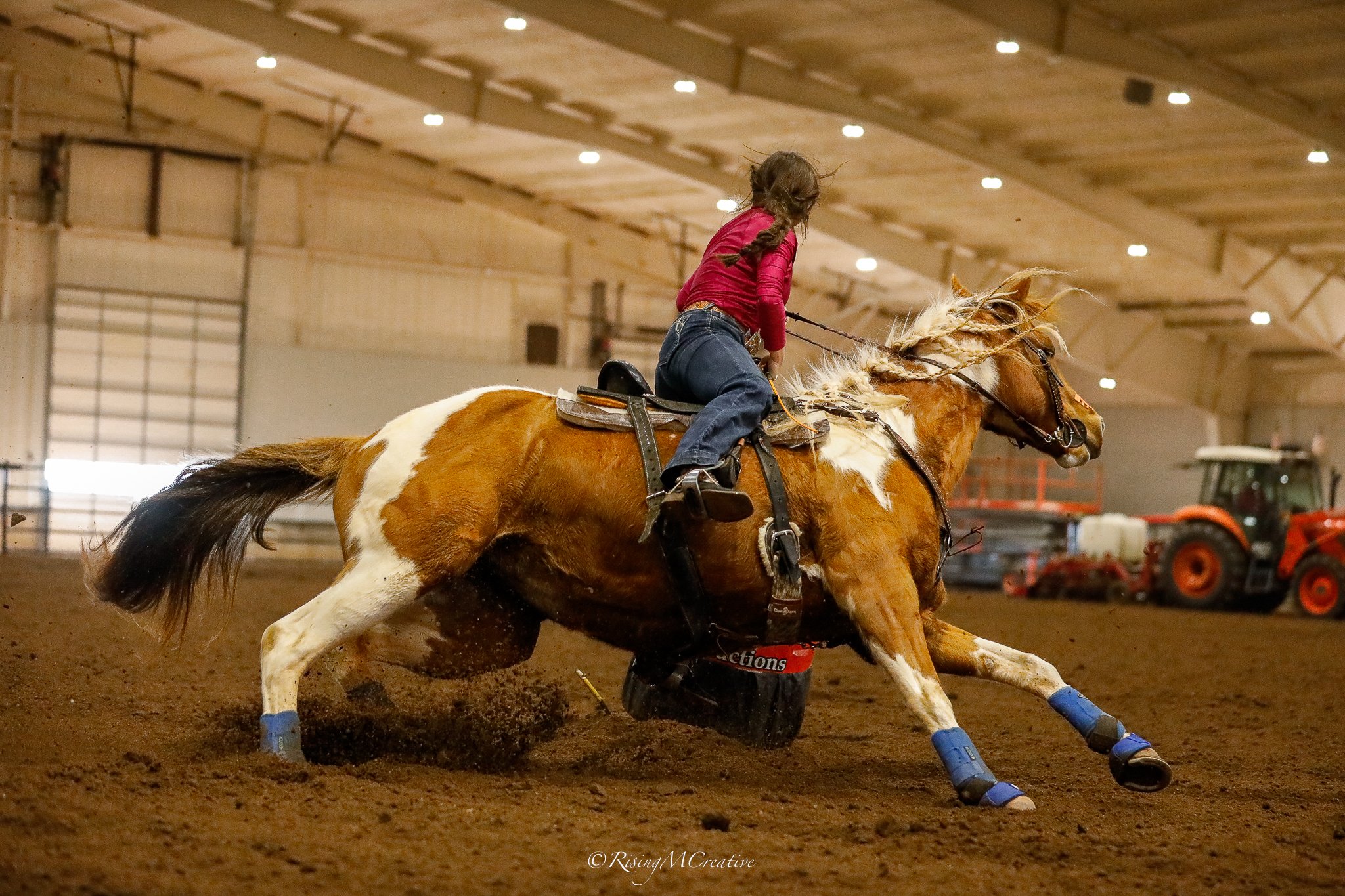 A person riding a bucking horse inside an indoor riding arena.