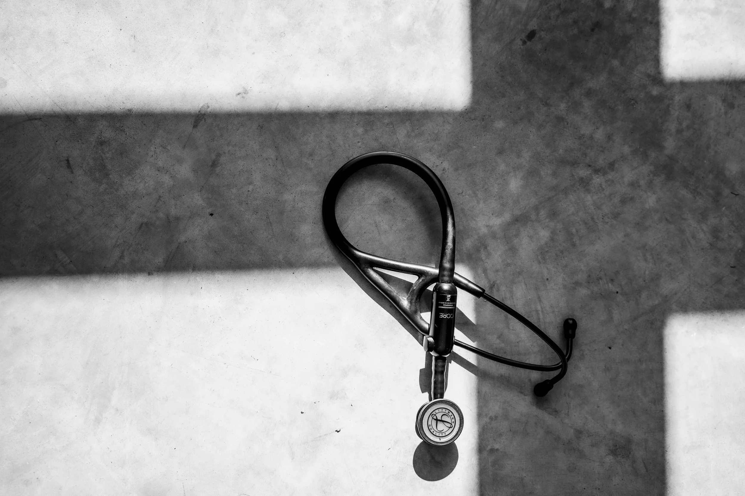 A stethoscope resting on a concrete surface, casting shadows in a black and white photograph.