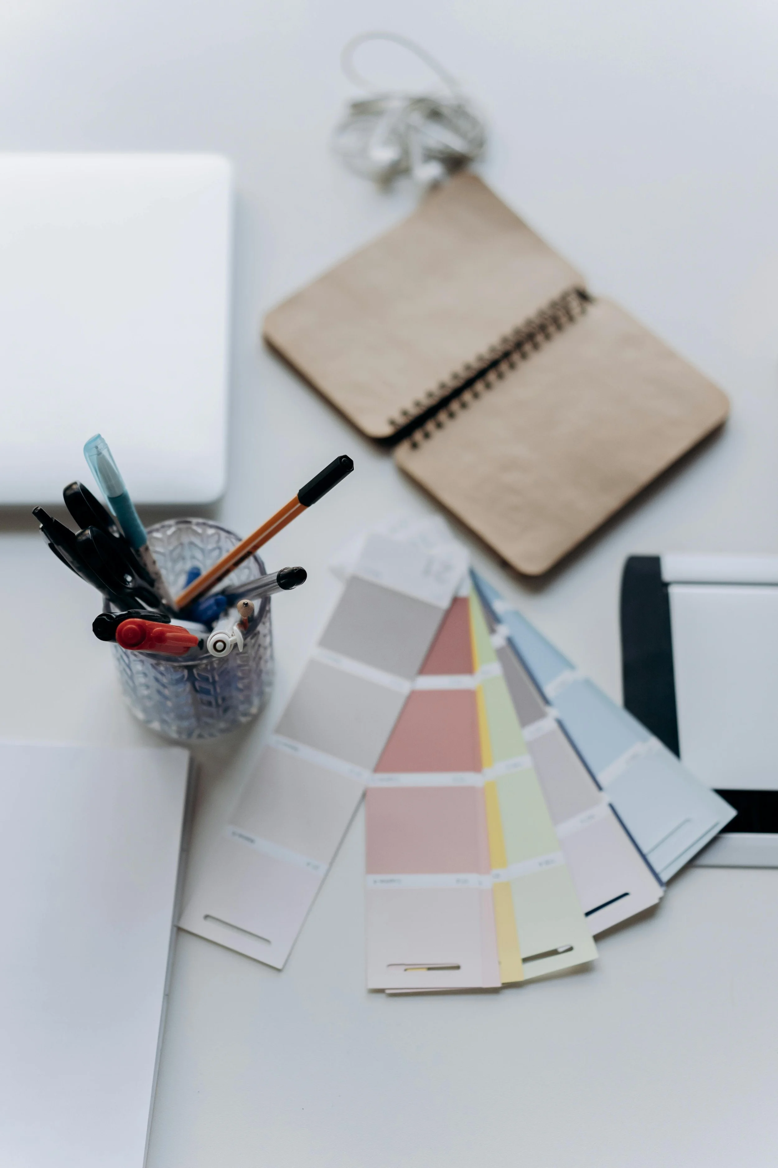 Desk with color swatches, pens in a holder, a notebook, and a laptop.