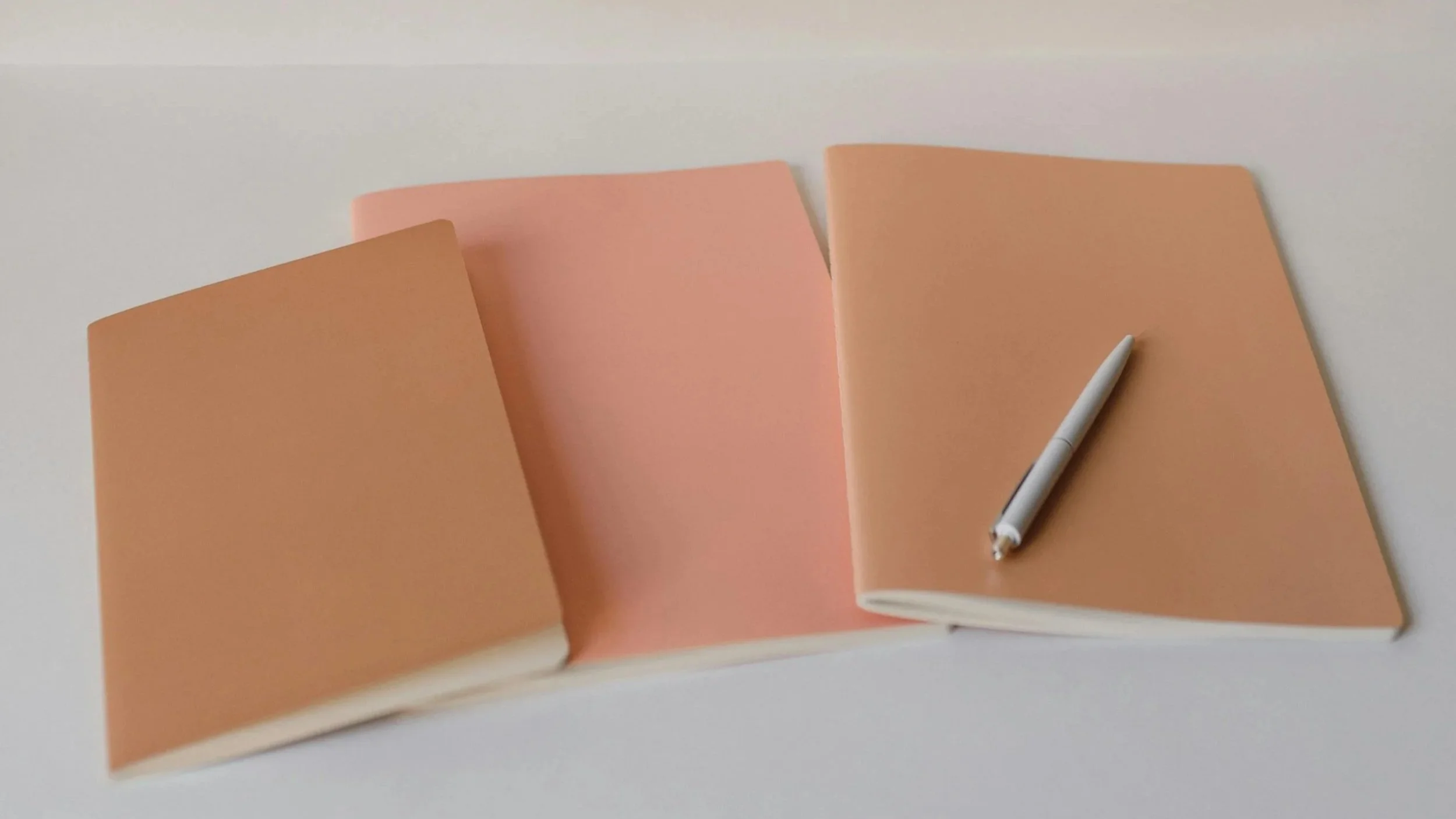Open notebook with peach-colored pages on white surface, with a silver pen resting on the right page.