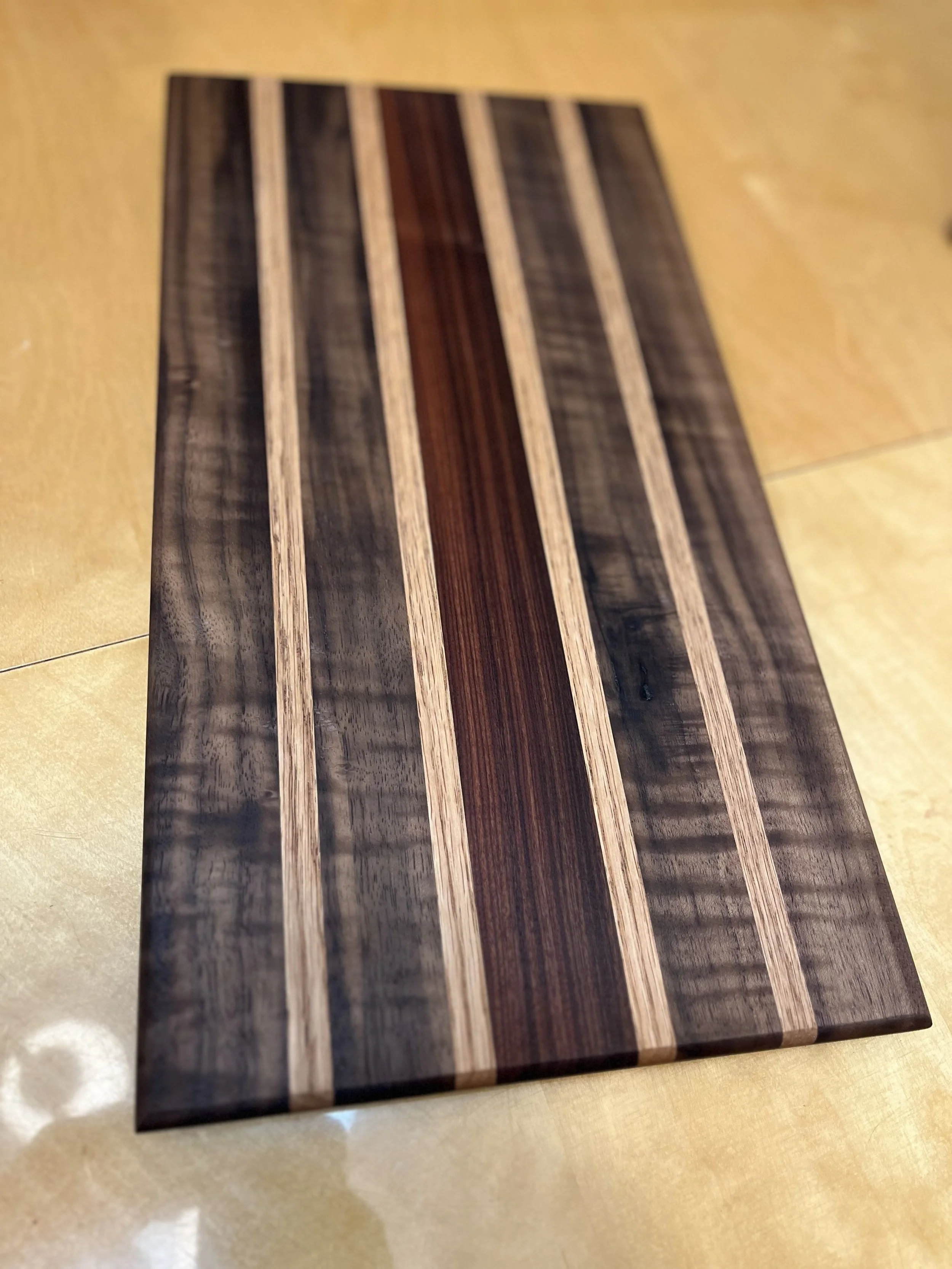 Wooden cutting board with vertical stripes of different shades of wood, on a beige surface.