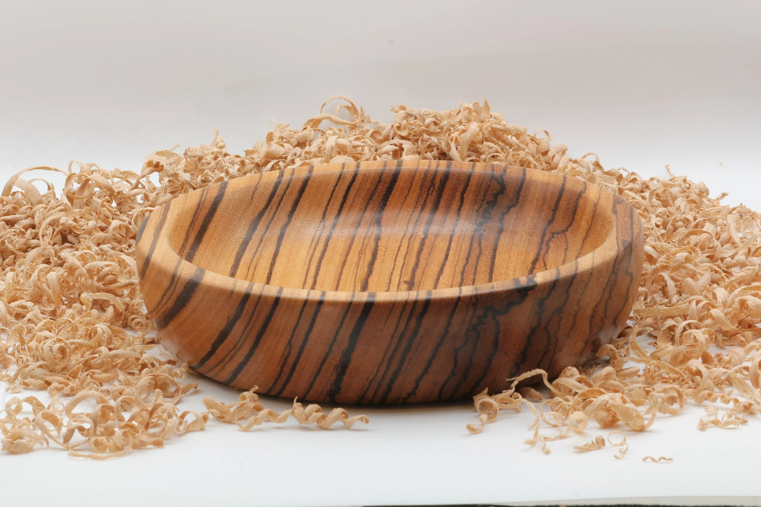 A wooden bowl on a white surface surrounded by wood shavings.