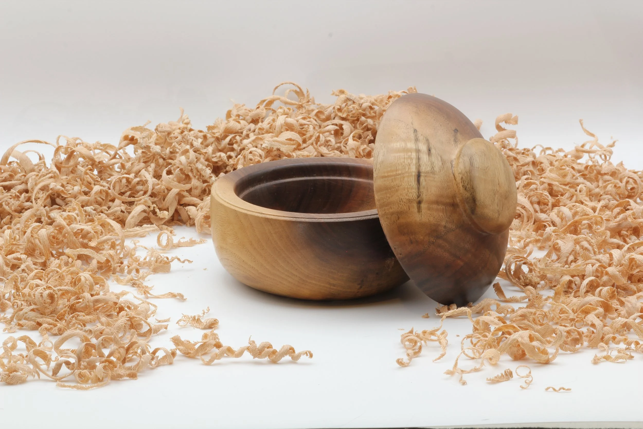 A wooden bowl and lid on a bed of wood shavings.
