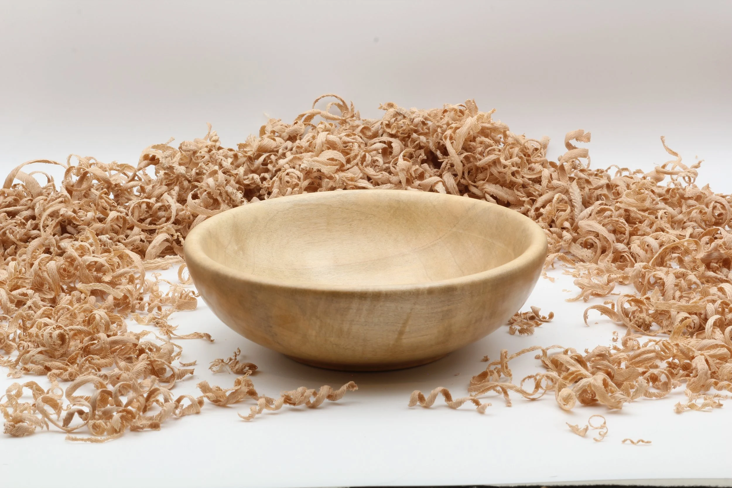 A wooden bowl surrounded by wood shavings on a white background.