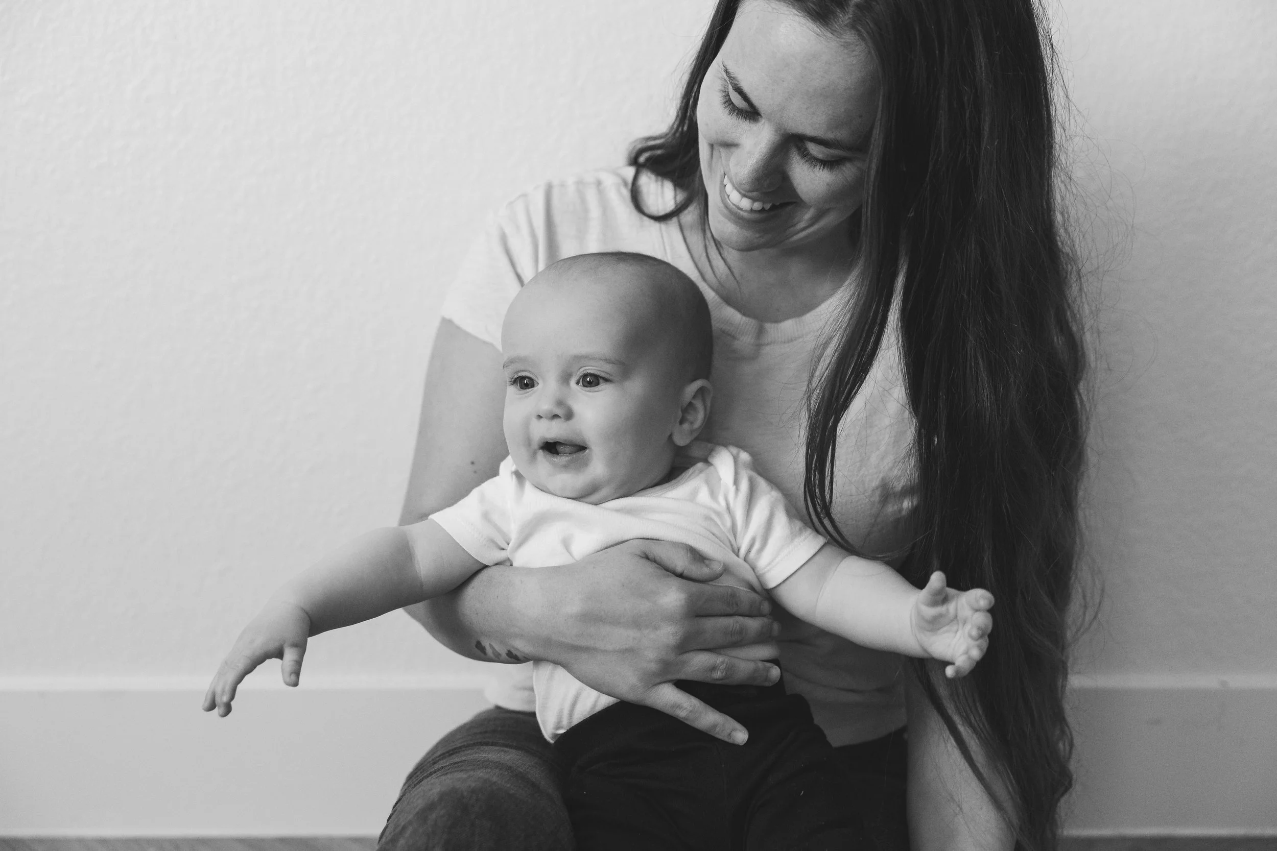 Black and white photo of a woman sitting on the floor, holding a baby on her lap, both smiling and looking at each other.