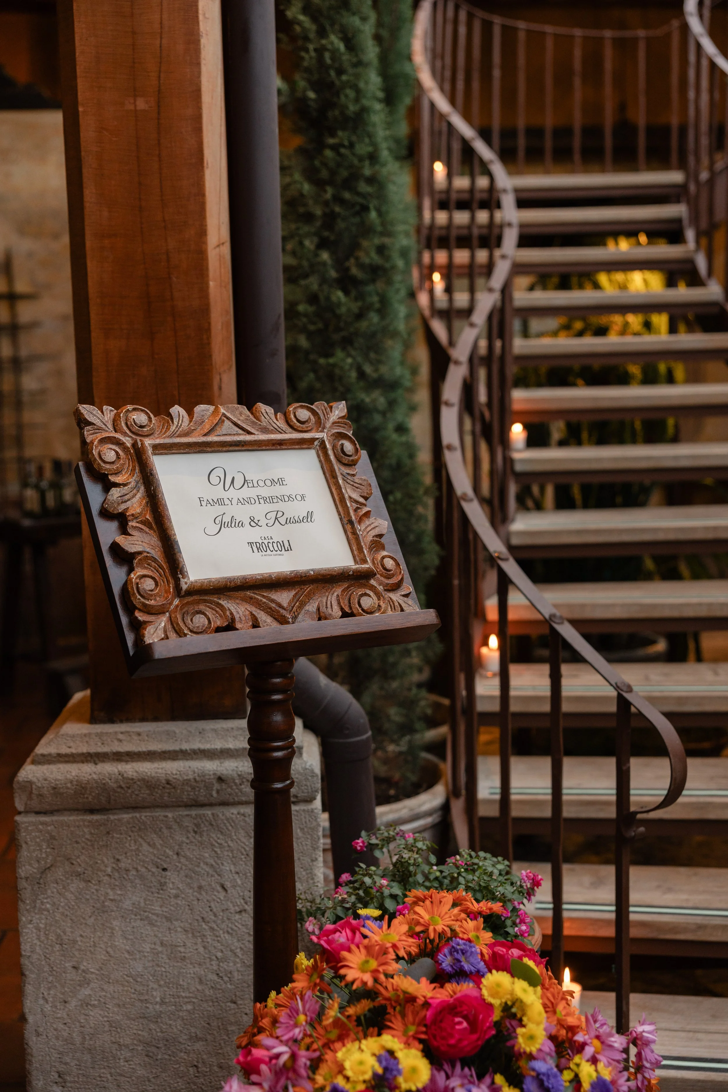 Welcome sign for family and friends of Julia and Russell at Casa Troccoli, with a staircase and flowers nearby.