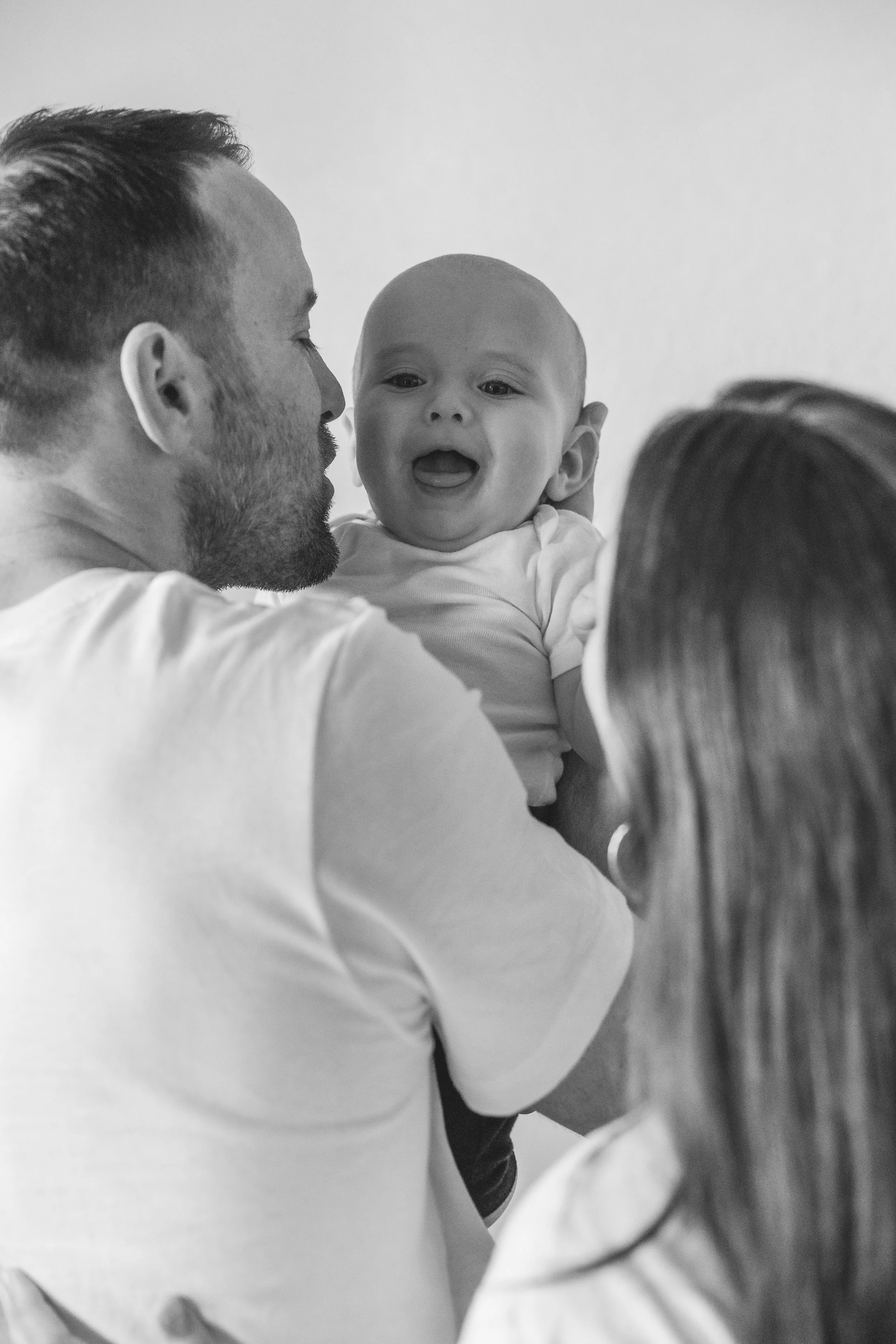 A man and woman holding a smiling baby together in black and white.