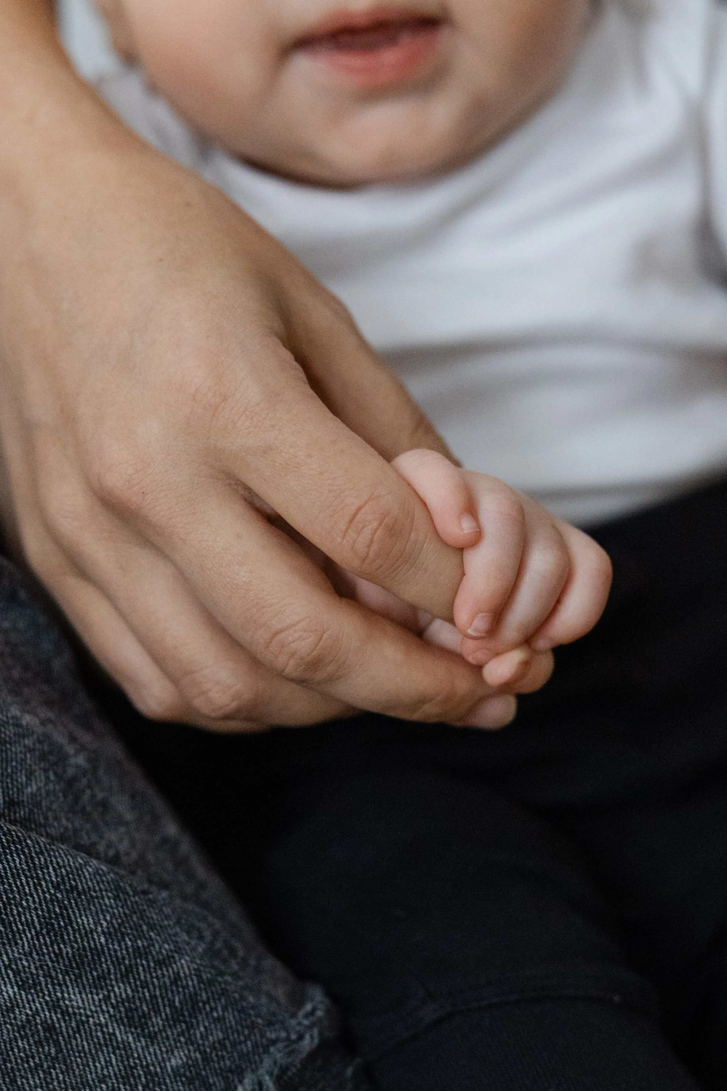 A close-up of an adult’s hand gently holding a child's hand, with the child's face partially visible in the background.