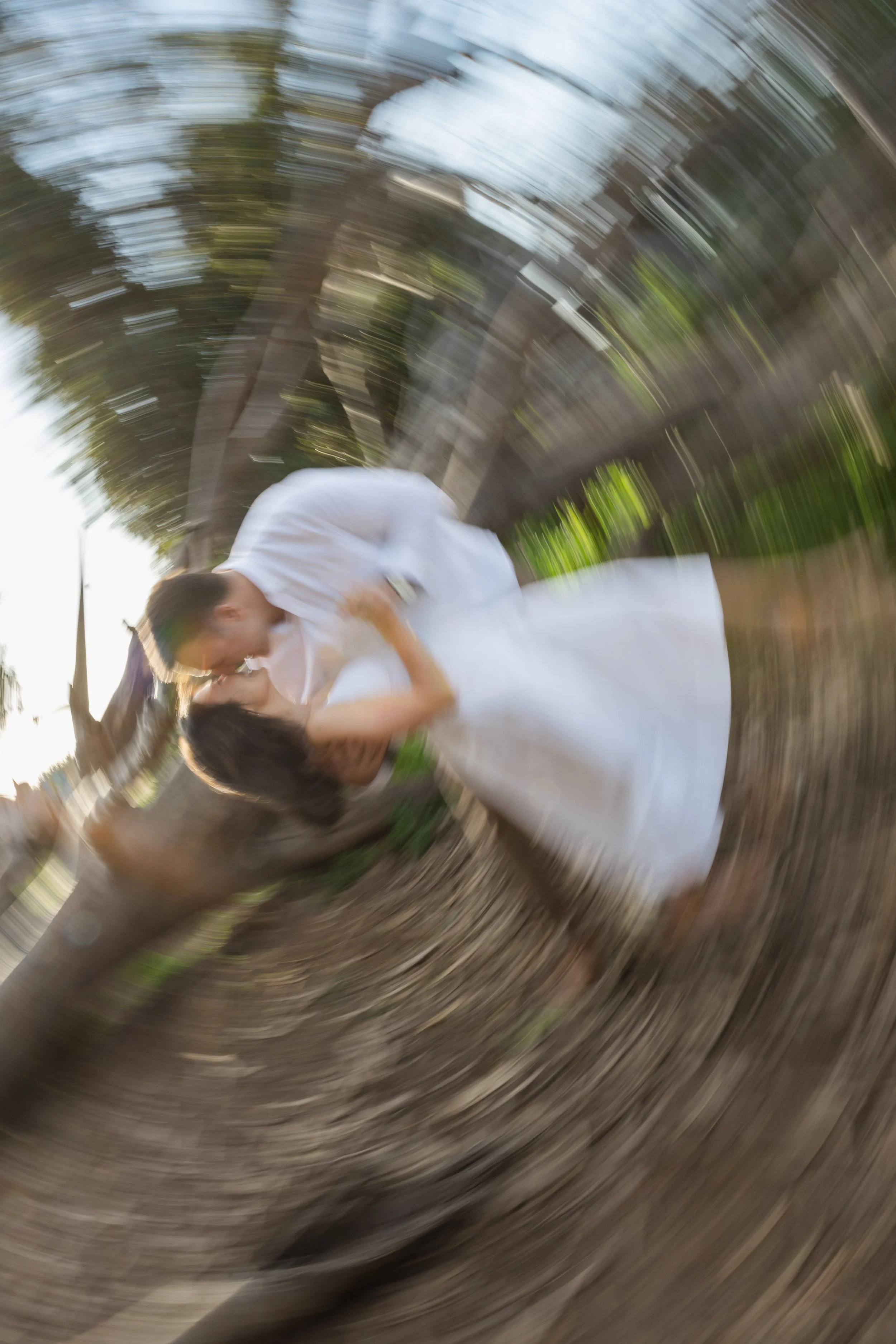 Couple kissing outdoors with a camera zoom effect, trees and a wooden fence in the background.