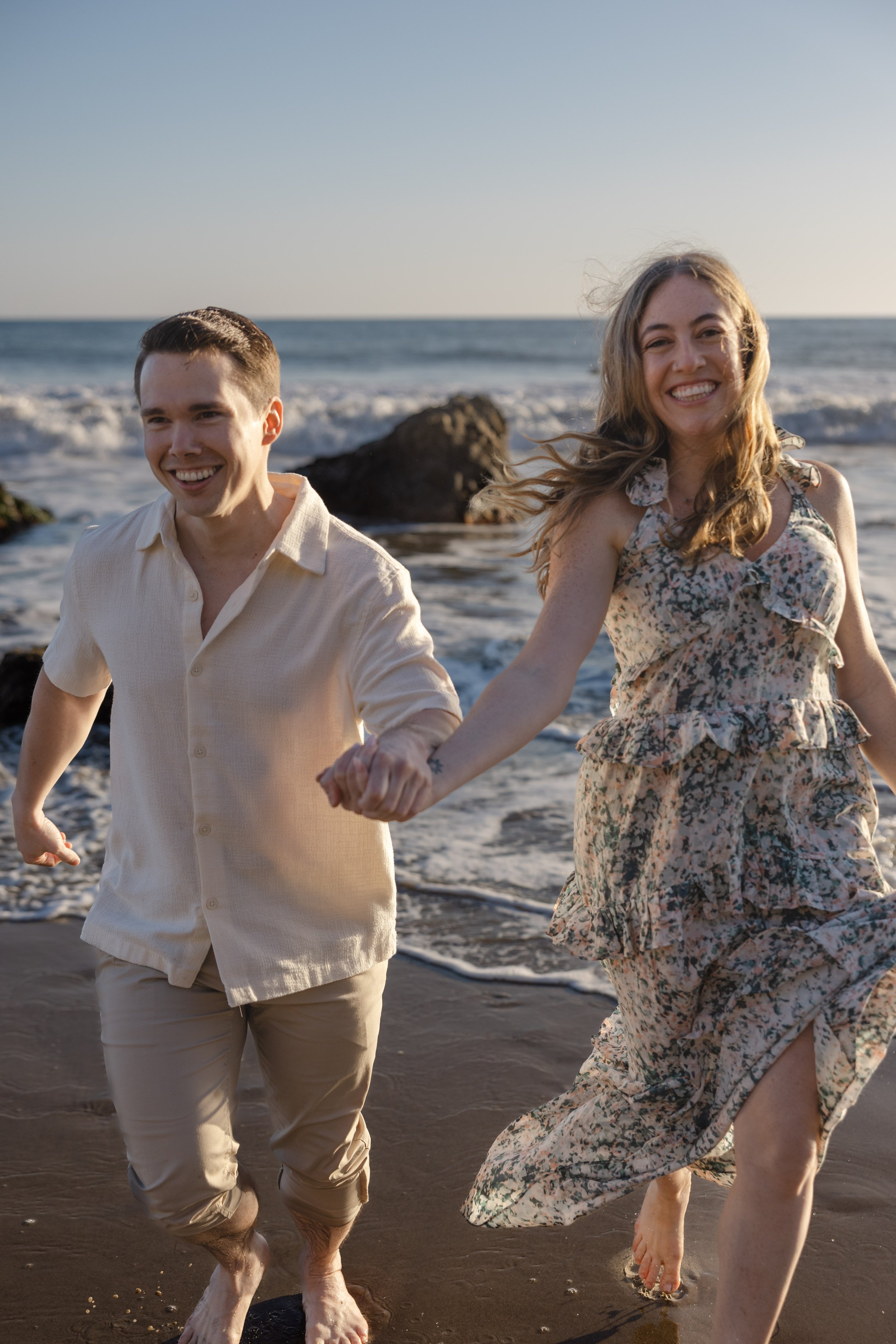 A smiling couple holding hands and running along the beach at sunset.