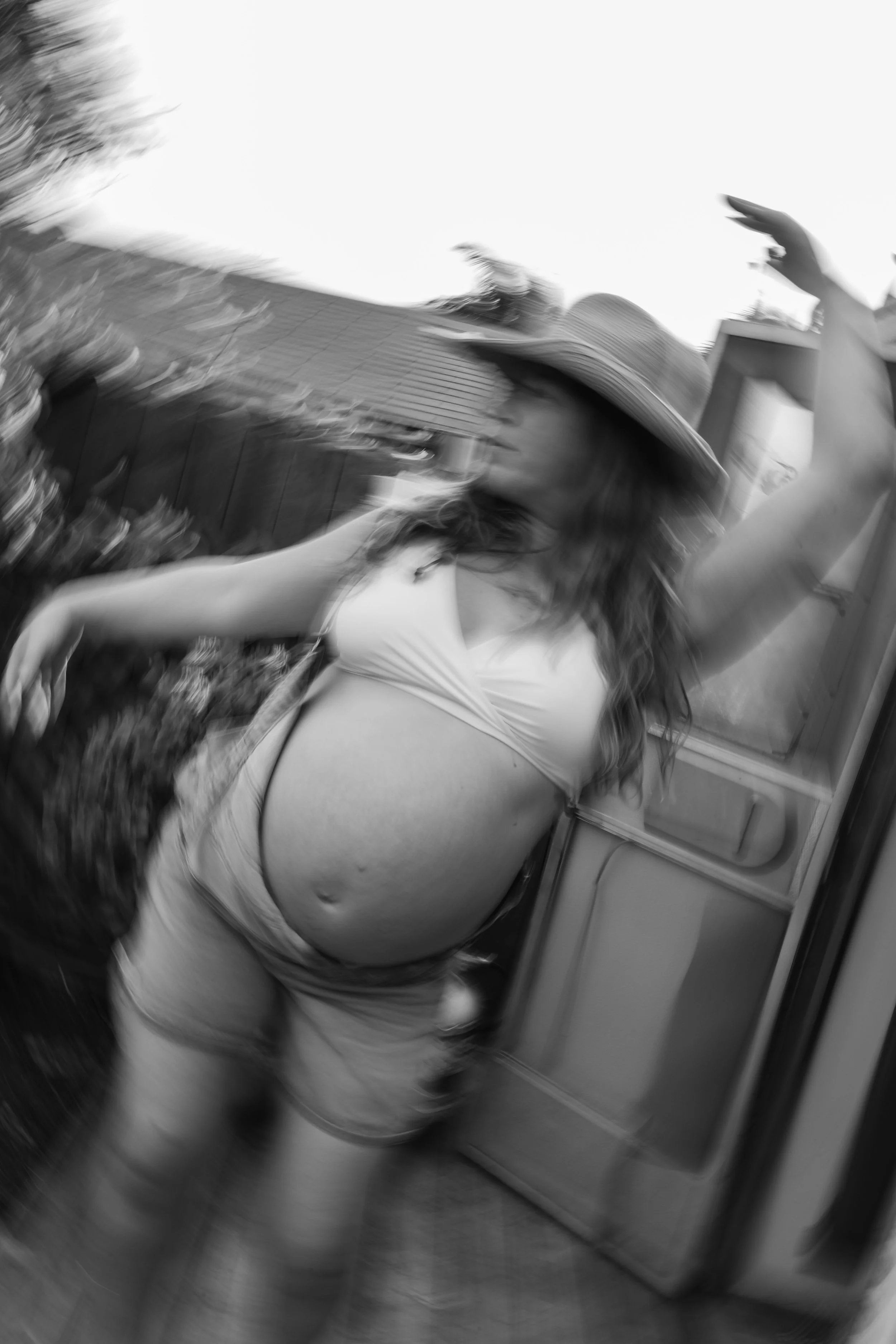 A woman with a hat and casual clothing standing inside a vehicle, possibly a bus or train, with her arm raised and a blurred background.