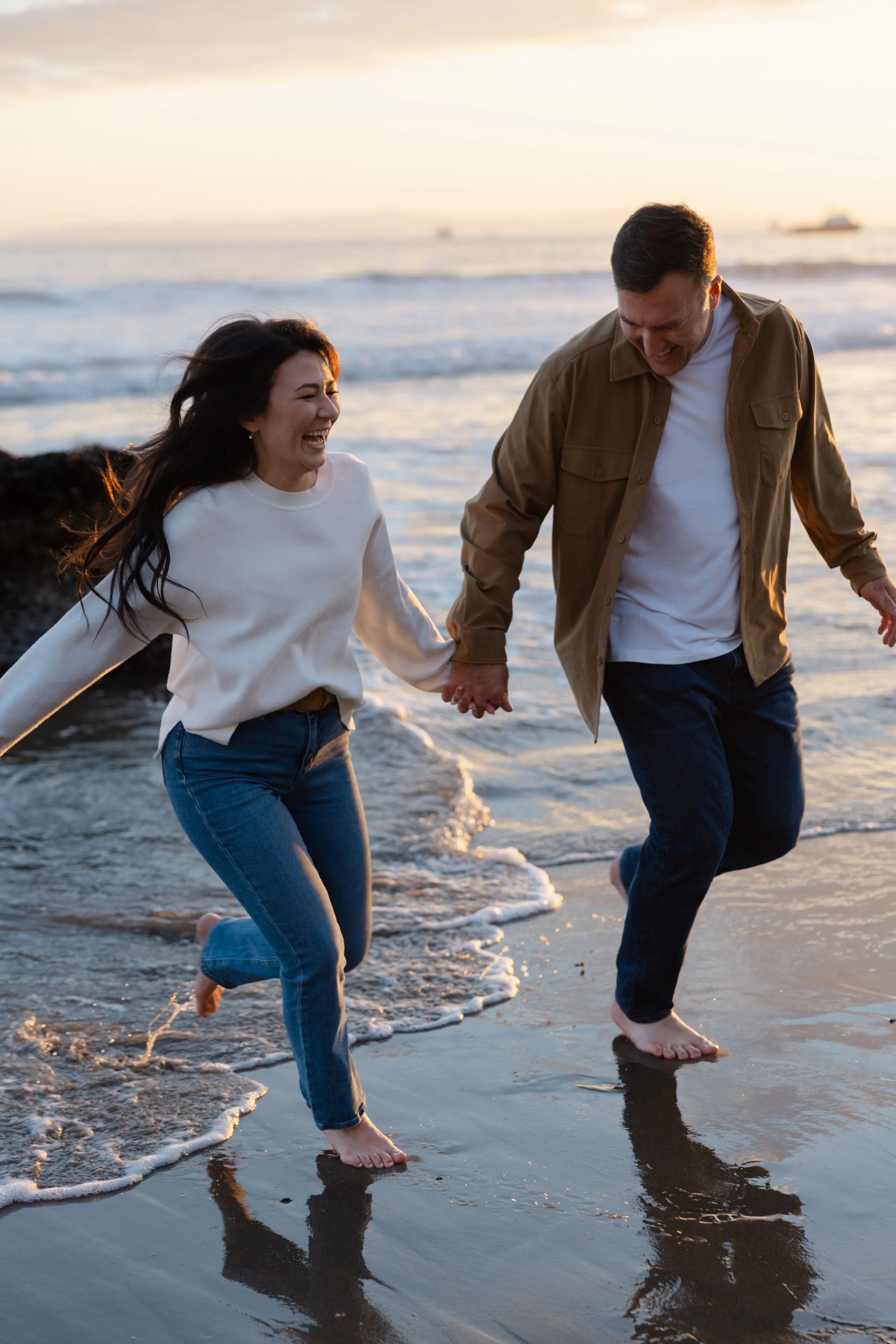 A happy couple holding hands and running on the beach at sunset