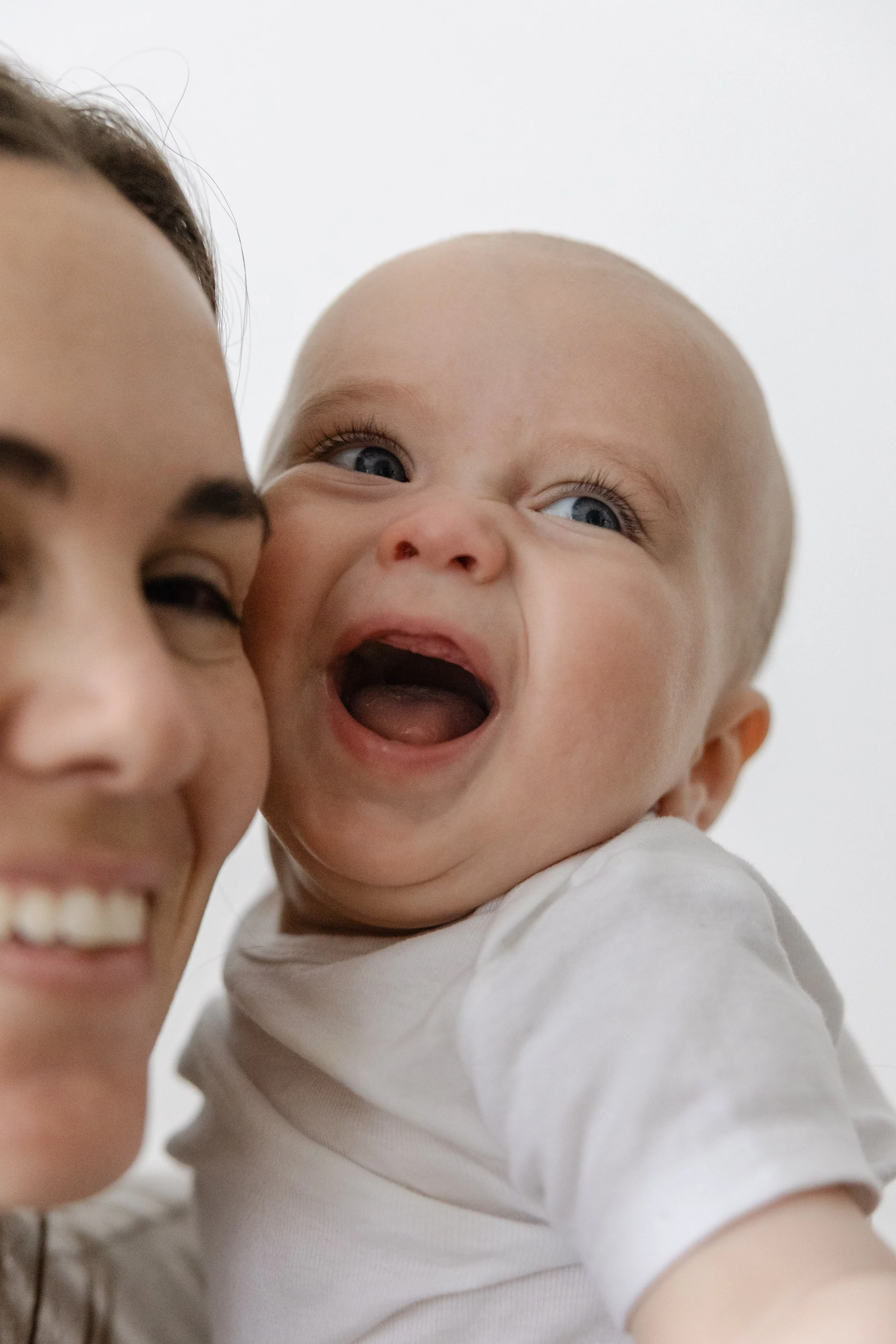 Close-up of a smiling woman and a happy baby with blue eyes, both appearing joyful.