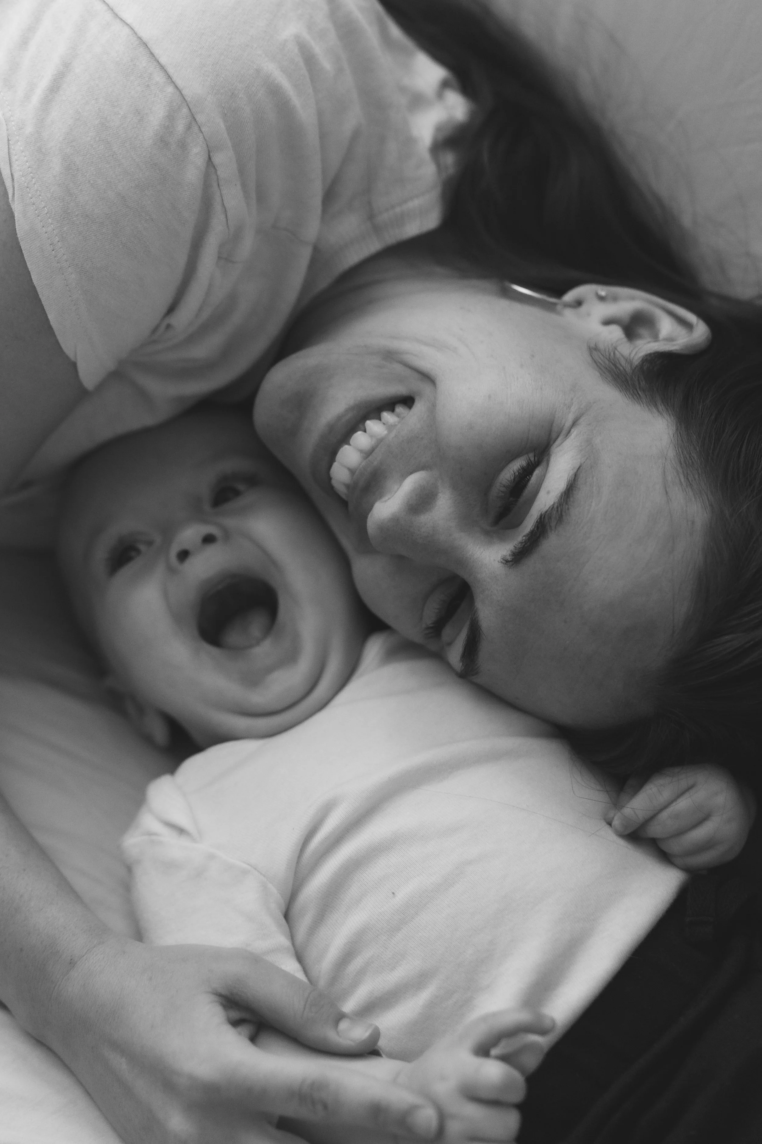 A woman and a baby lying down together, both smiling and laughing, in a black and white photo.