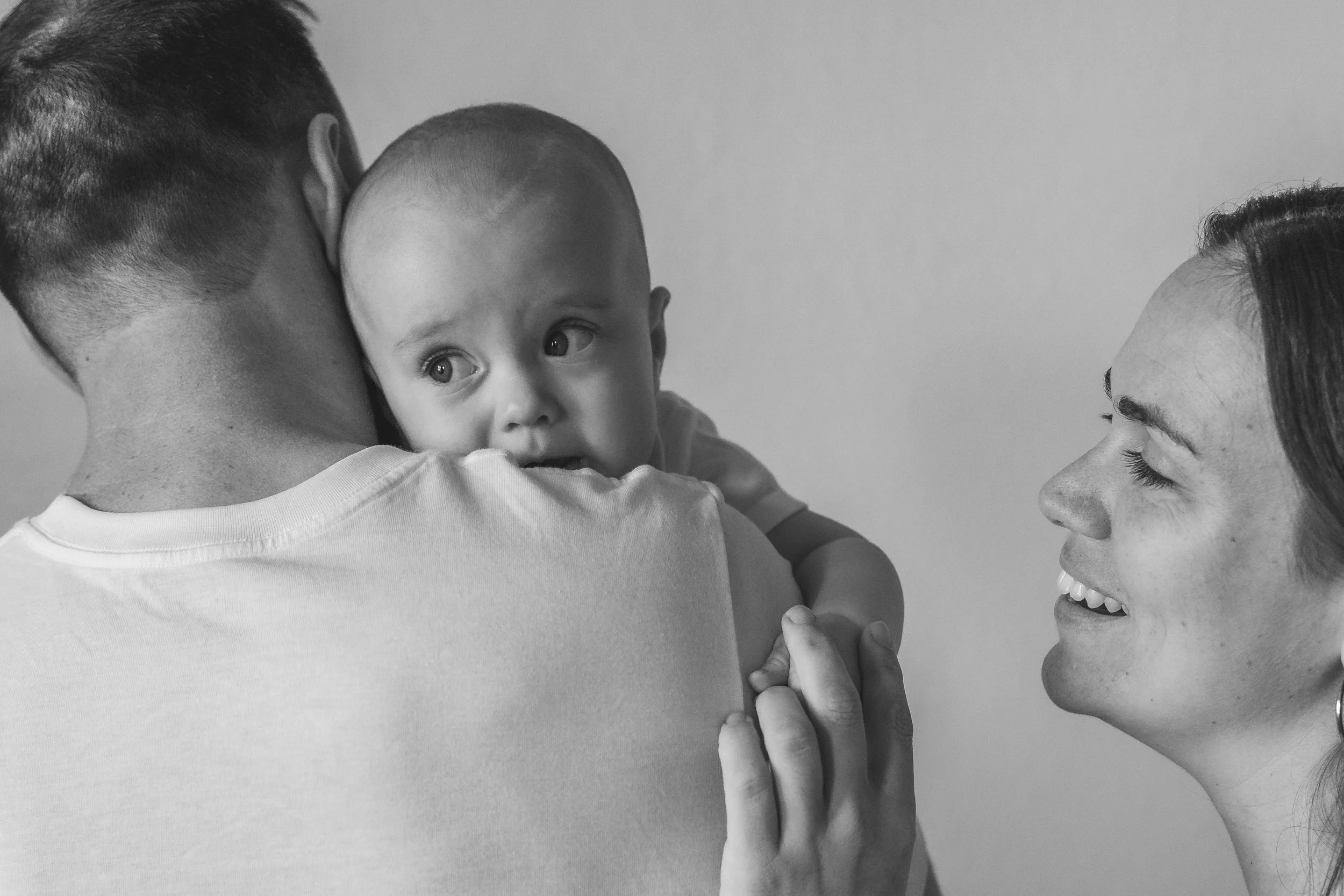 A person holding a baby while a woman looks at them with a smile
