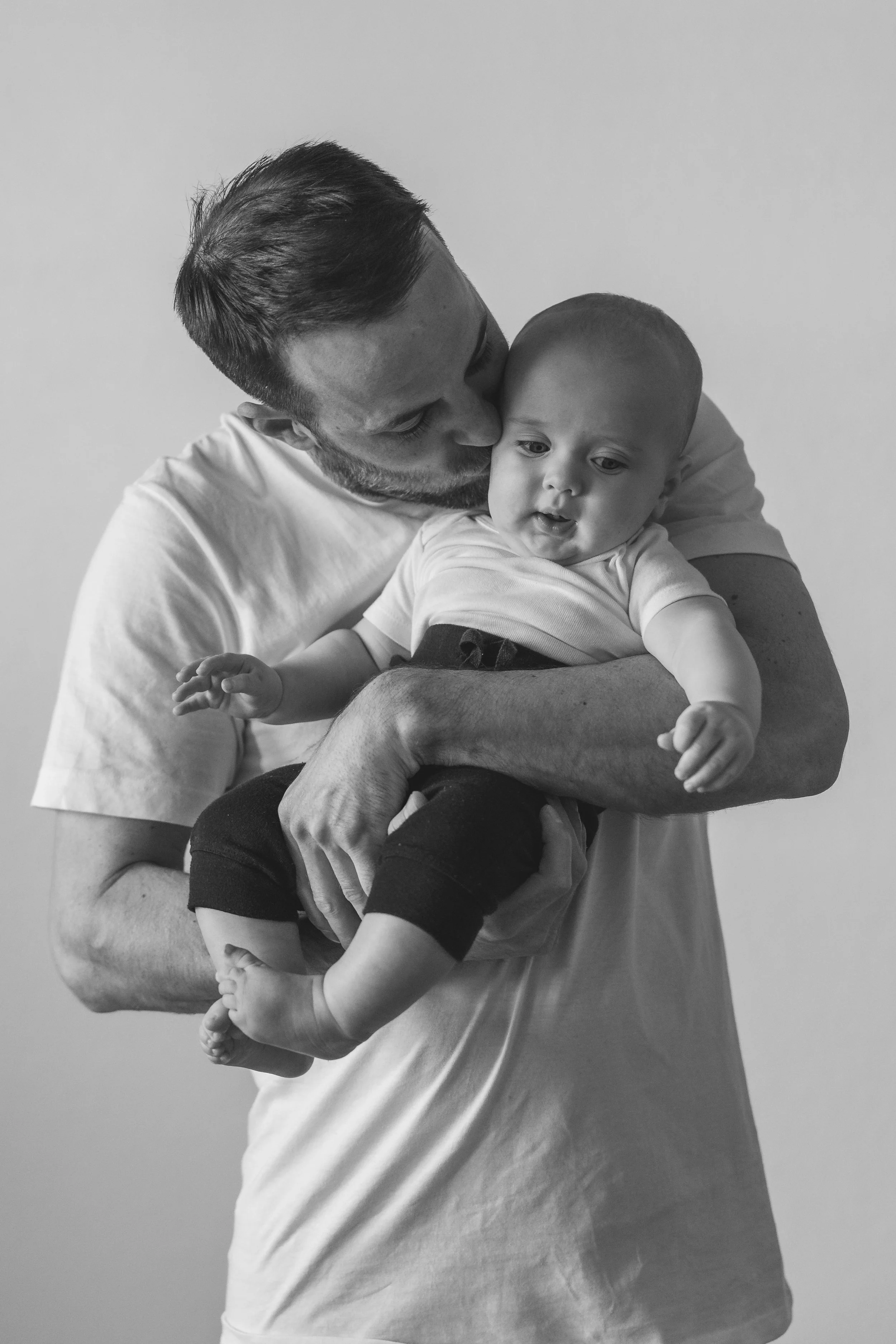 Black and white photo of a man holding and kissing a baby.