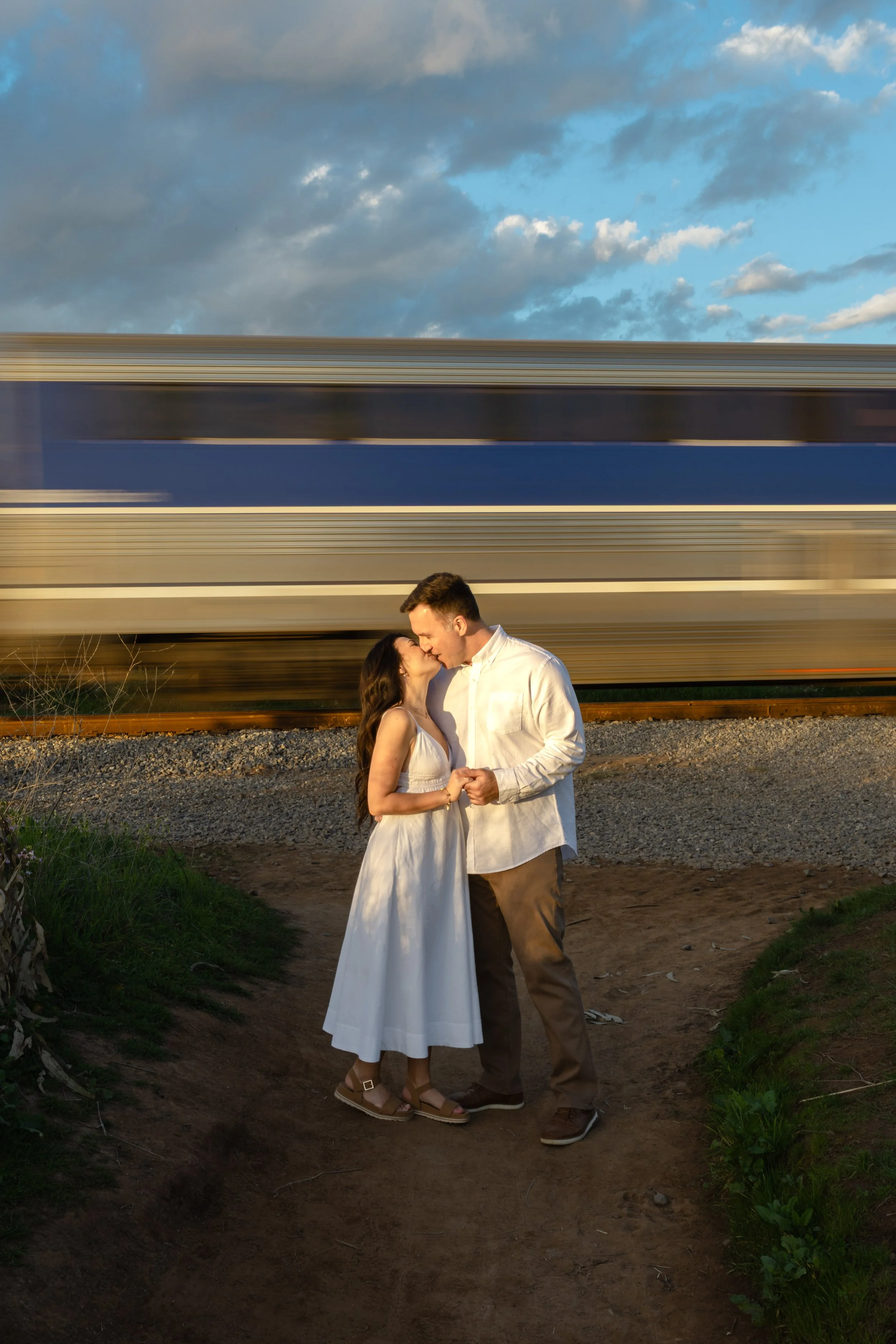 A couple dancing outdoors at sunset with a moving train in the background.
