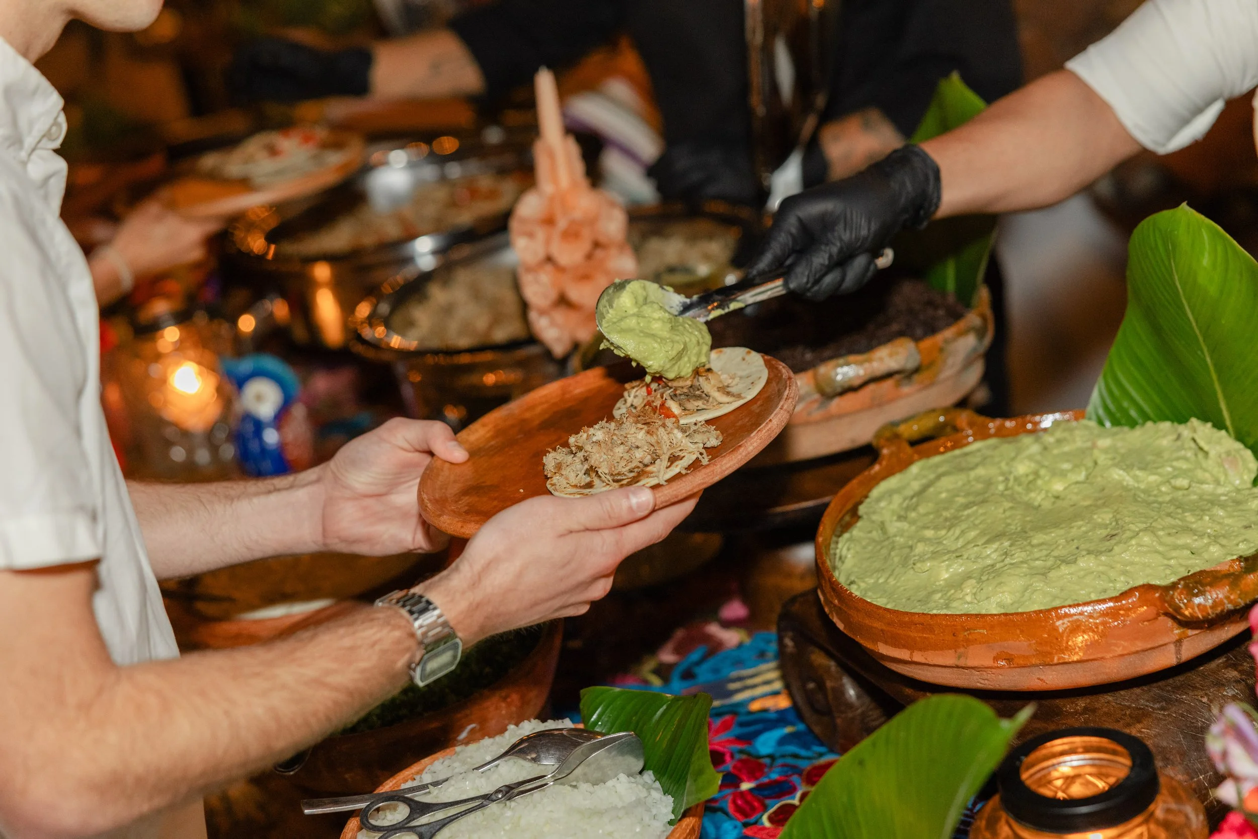 People serving and receiving traditional Mexican food with guacamole, shredded meat, and rice at a lively food stall.