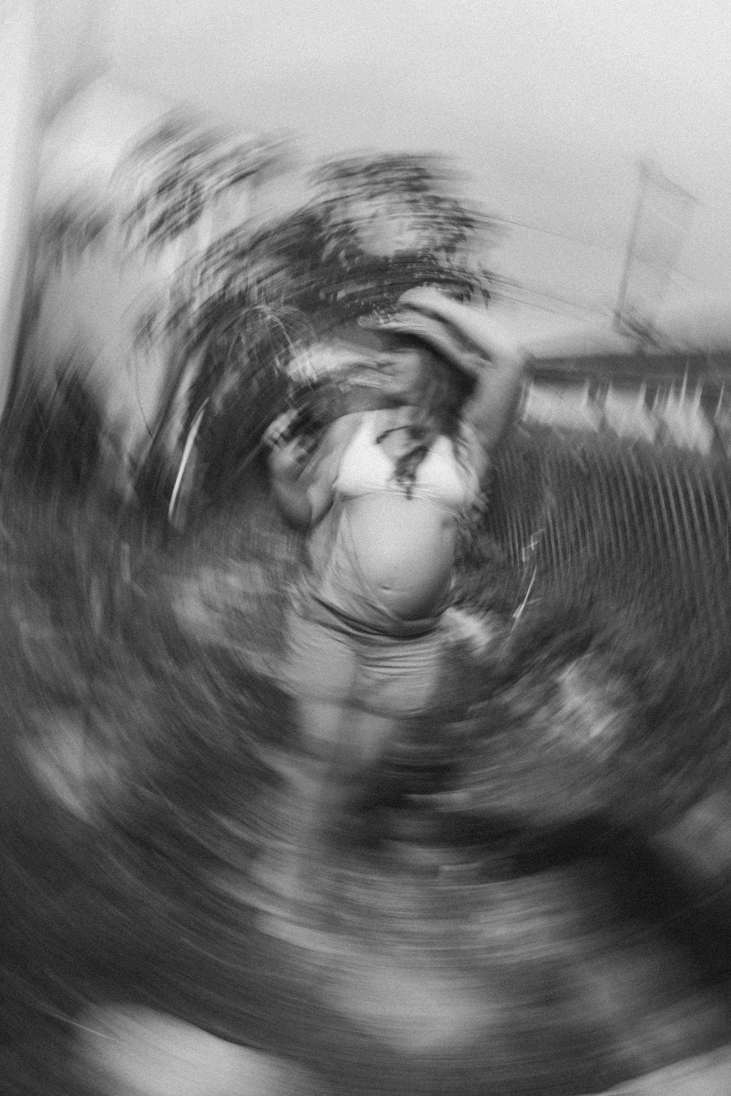 Blurry black and white photo of a person holding their stomach, possibly pregnant, with a distressed expression, standing near a textured wall or fence.