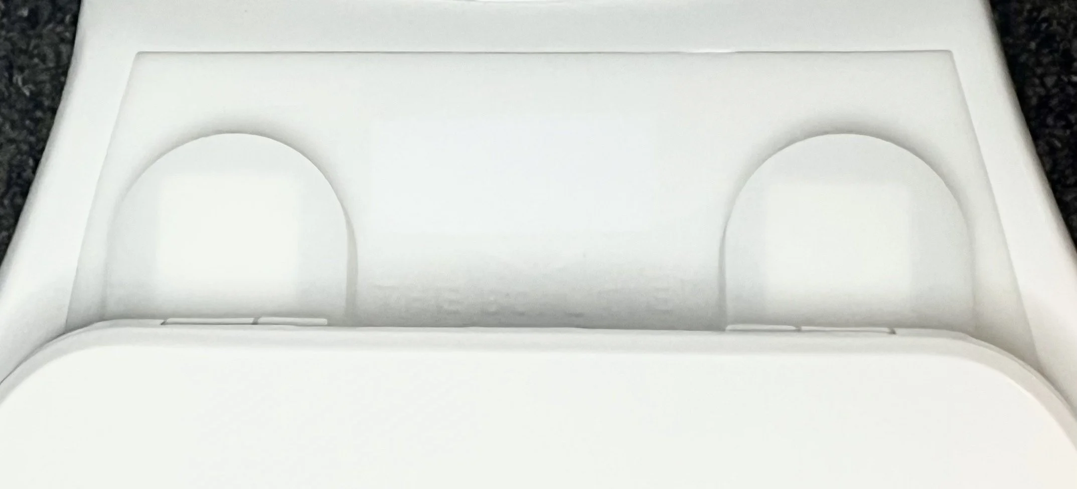 Close-up of the Bowl Tie in place at the back of the toilet seat, over the bolts covers.  The Bowl Tie blocks moisture and grime from getting in those hard to clean places.