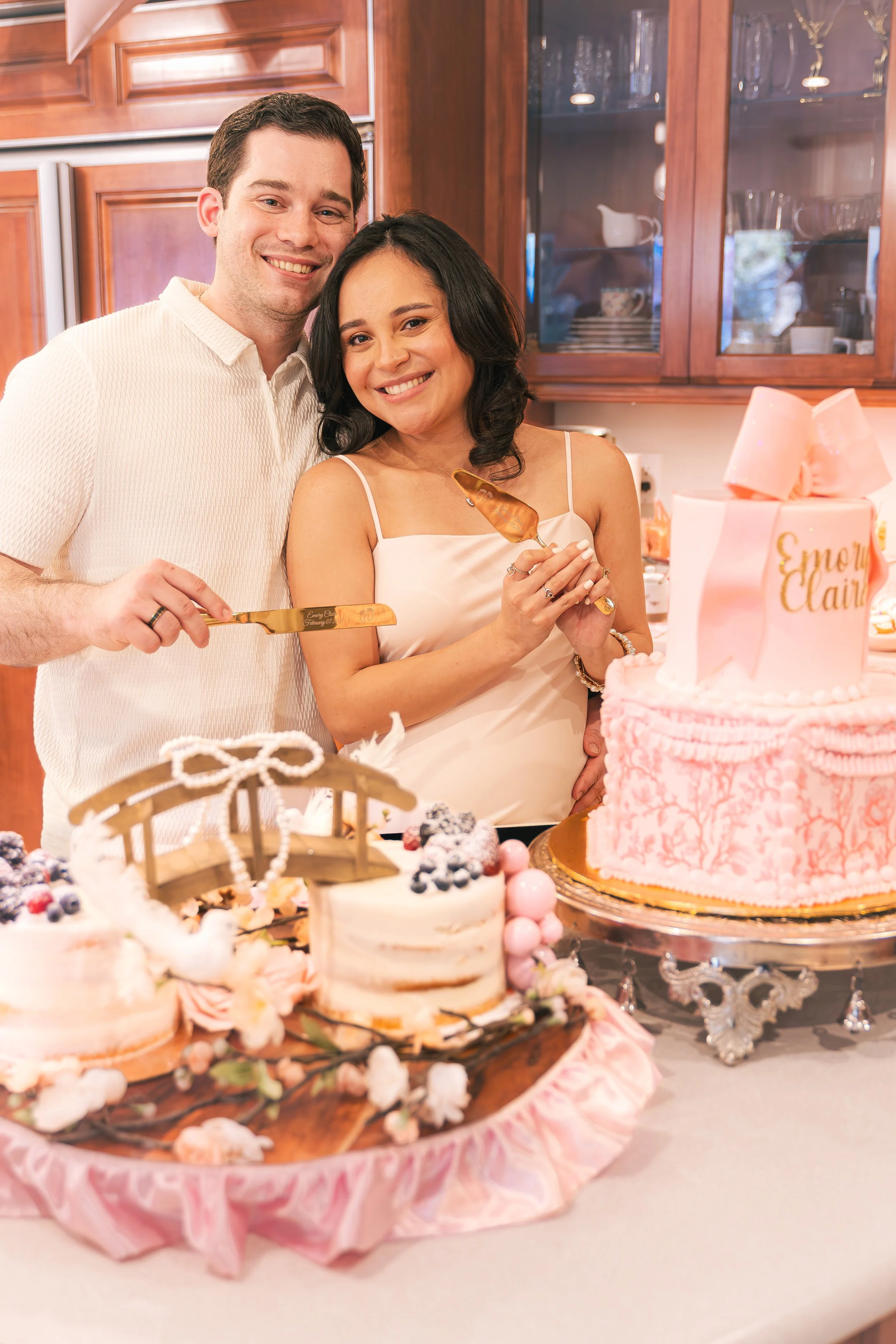 A man and woman smiling while cutting a pink birthday cake at a celebration.