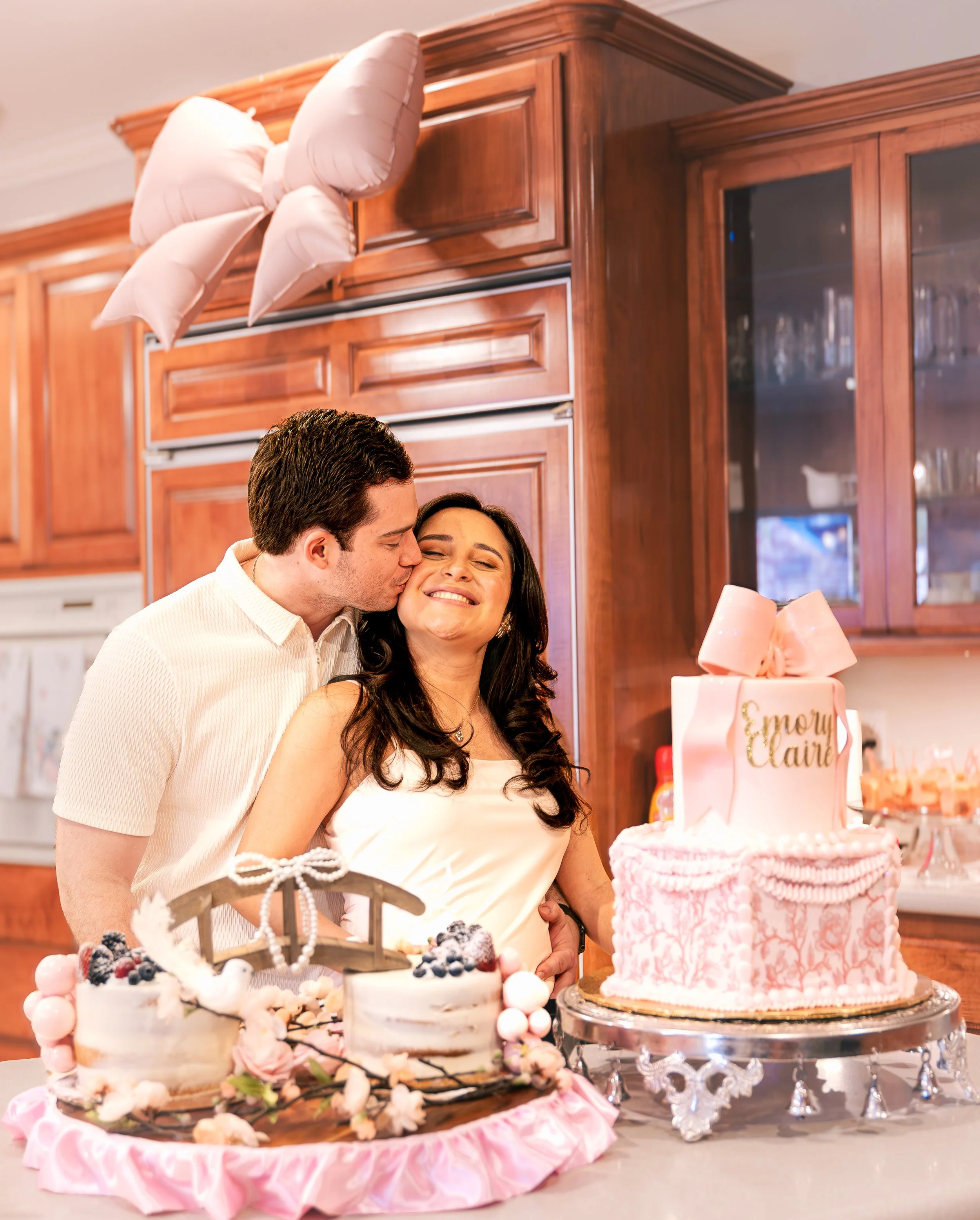 A couple celebrating a wedding or special occasion with desserts and a cake, in a room with wooden cabinets.