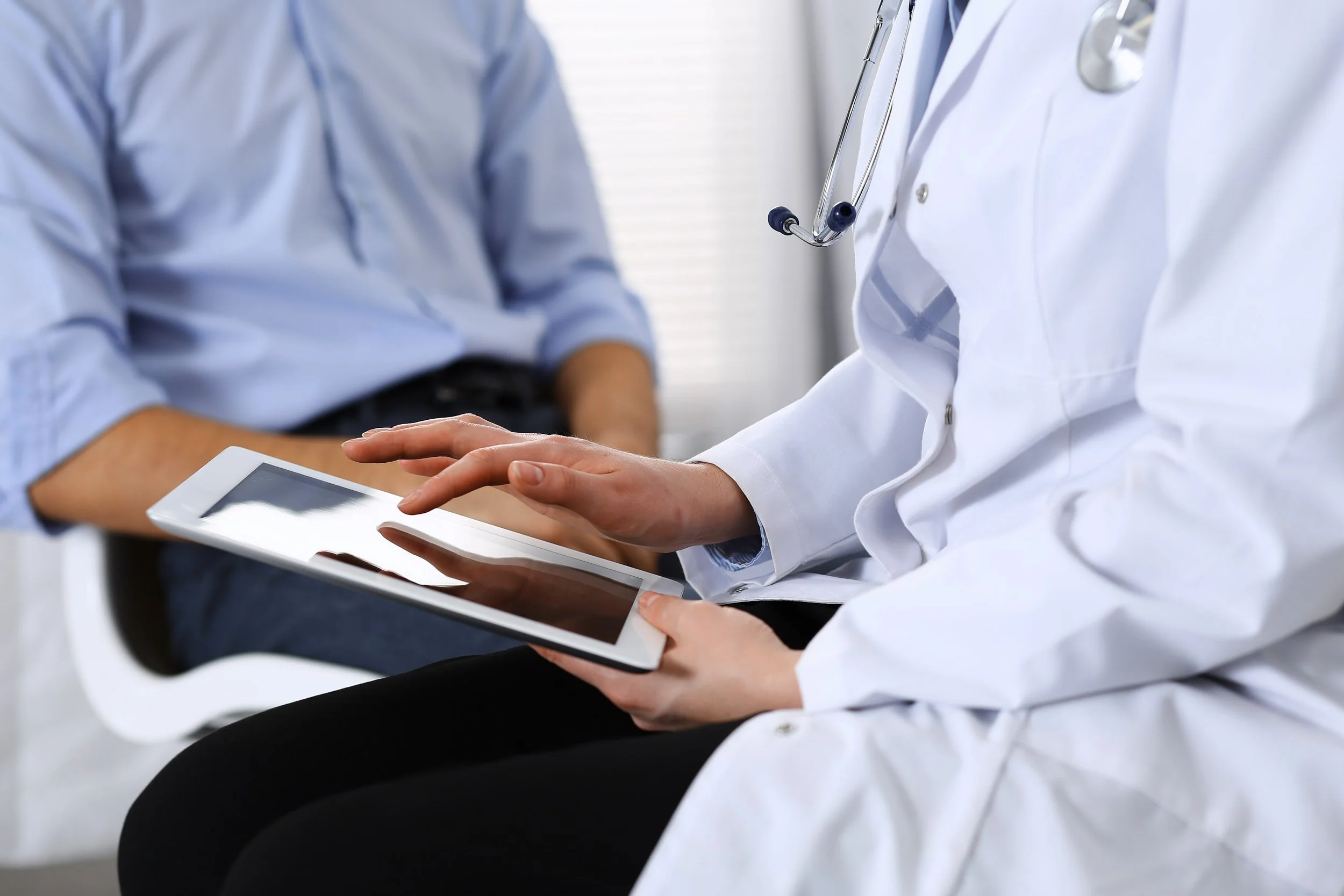 A doctor showing a patient something on a tablet in a medical setting.