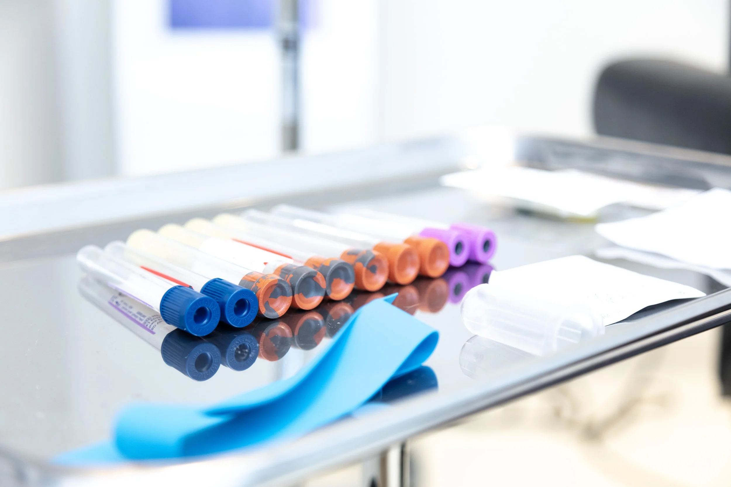 Collection of unused medical test tubes with colored caps on a metallic medical table in a clinical setting.