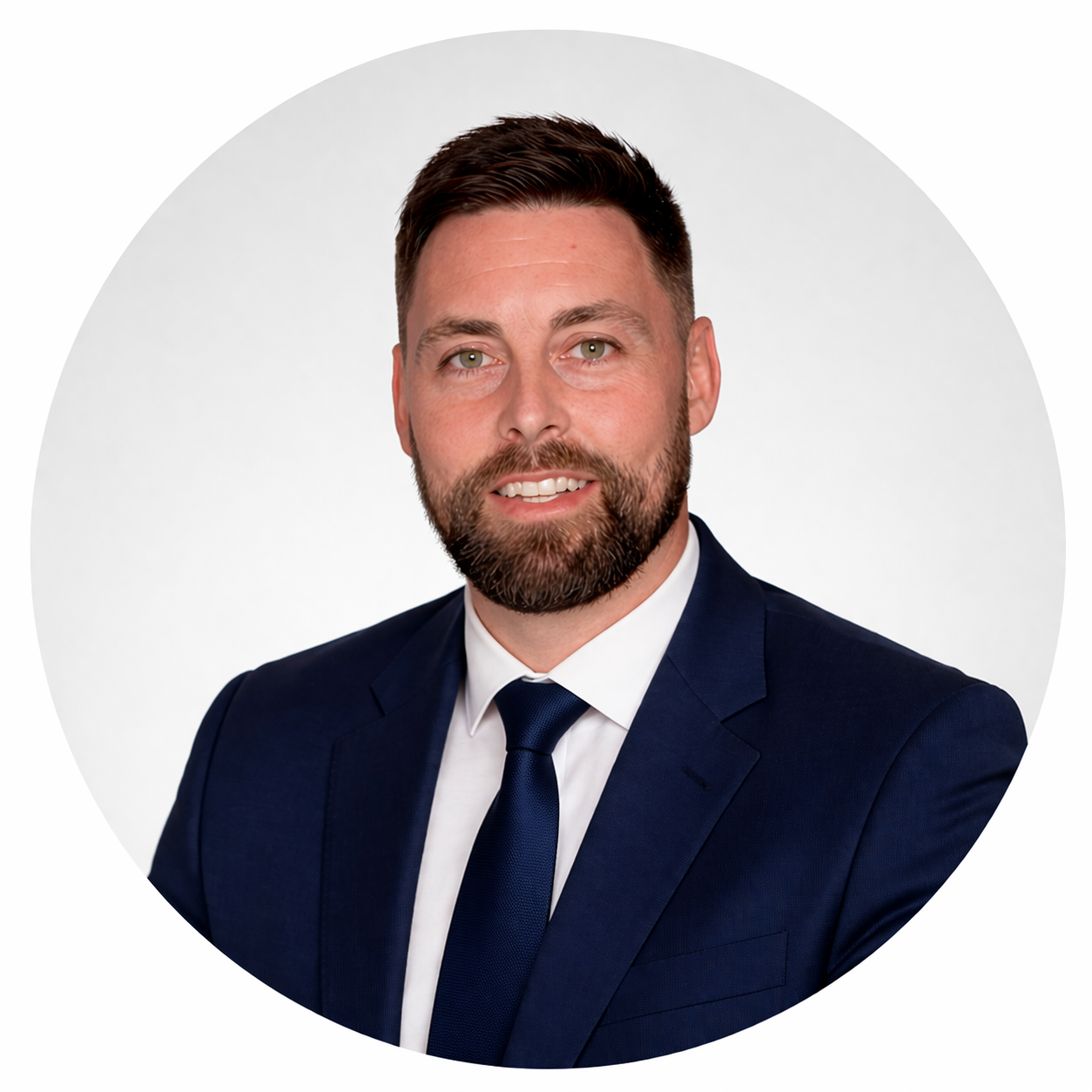 Professional headshot of a man with short dark hair and a beard, wearing a navy blue suit, white shirt, and navy tie, smiling against a plain white background.