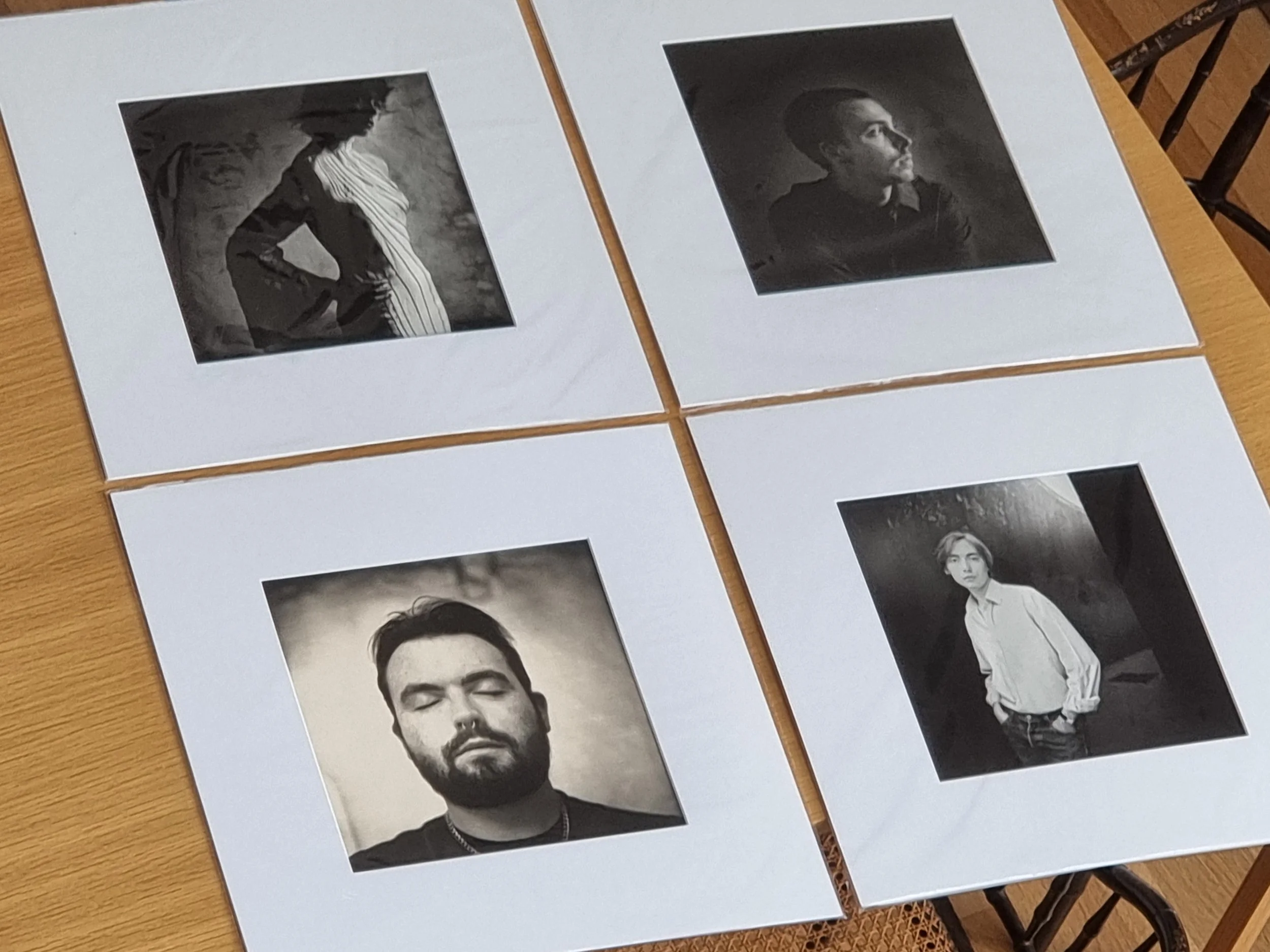 Photographies en noir et blanc de quatre personnes, posant dans différents styles. Disposées sur une table en bois, chaque photo est encadrée par une marge blanche.