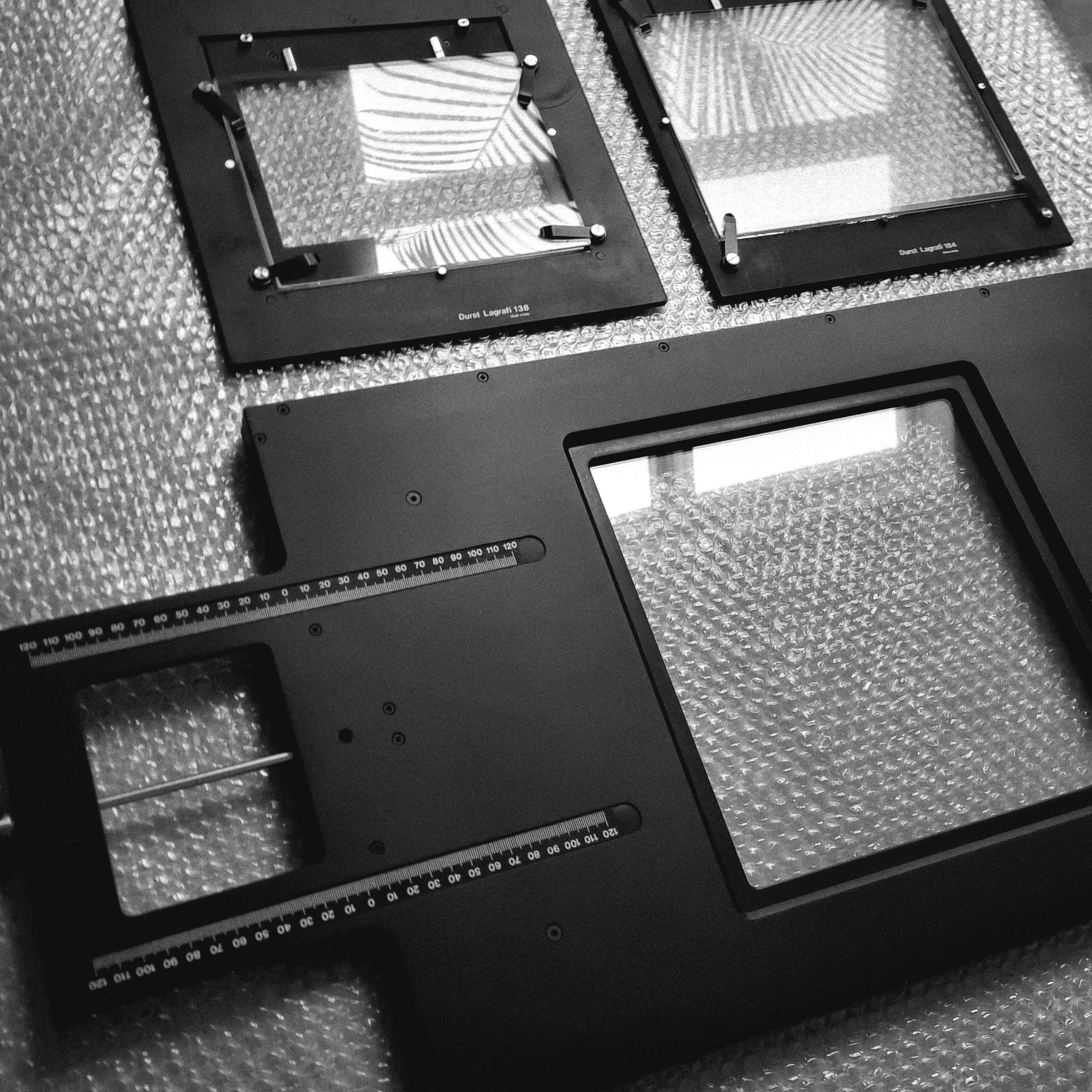 Deux cadres en plastique avec des vitres en verre et des échelles de mesure, posés sur un tapis en mousse à bulles.