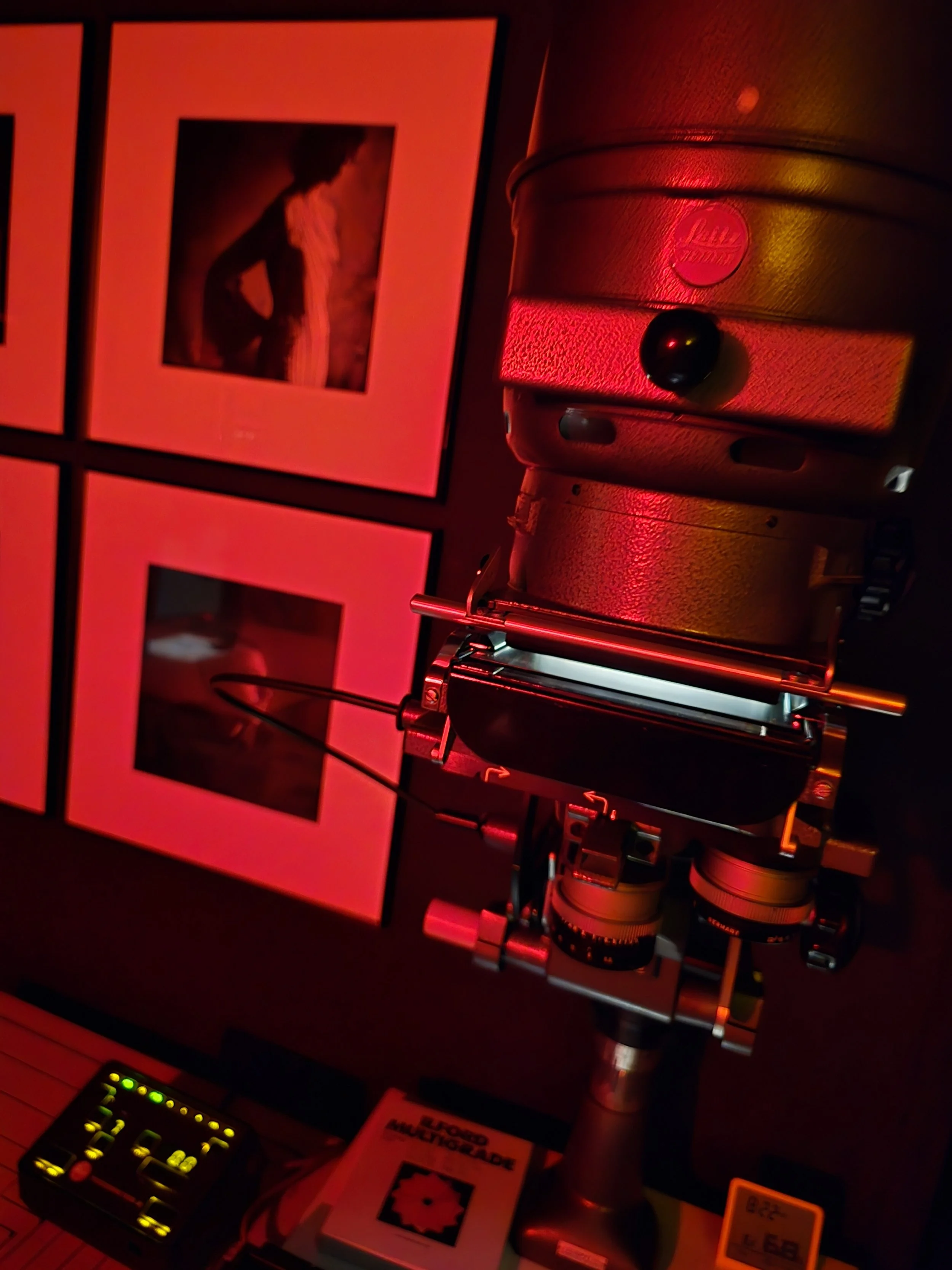 Agrandissuer dans une chambre noire, illuminée par une lumière rouge, avec des portraits en arrière-plan.