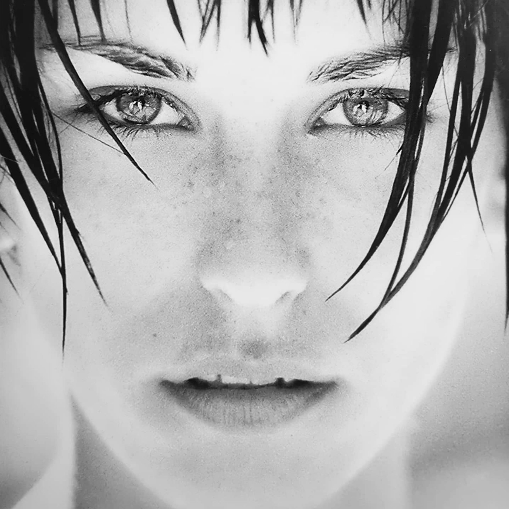 Un portrait en noir et blanc d'une jeune femme avec des cheveux noirs, aquatiques, et un regard intense, avec des détails en gros plan sur ses yeux et ses lèvres.