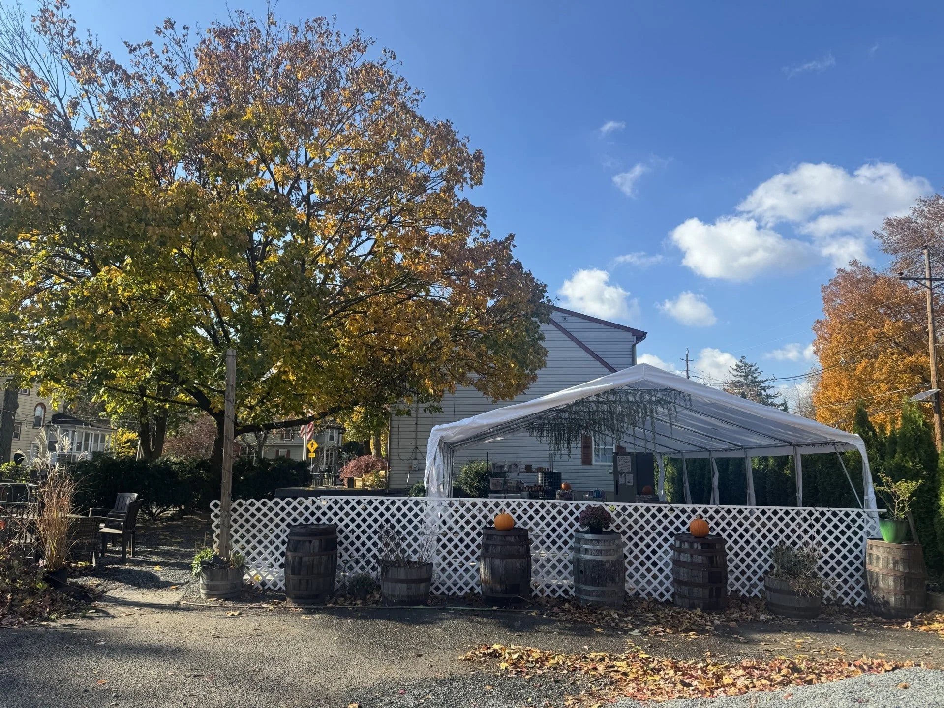 An outdoor scene with a white tent decorated for fall, set against trees with autumn foliage on a sunny day with a blue sky. A perfect outdoor venue for guests at your Eclipse Brewing event.