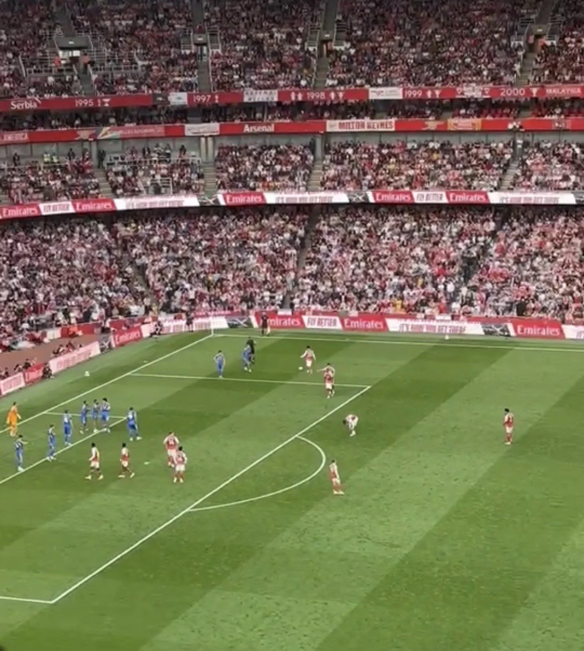 A soccer match underway in a stadium filled with spectators, with players on the field and advertisements around the sidelines.