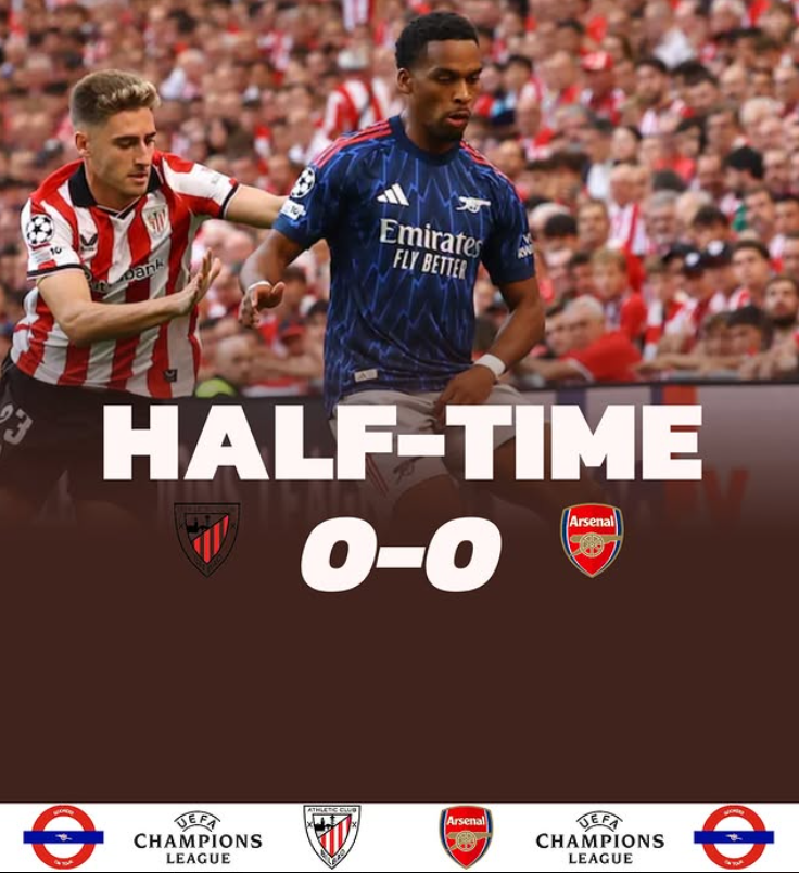 Photograph of two soccer players during a match, with crowd in the background. The scoreboard shows it is halftime with a score of 0-0 between Atlético Madrid and Arsenal. The image includes UEFA Champions League branding.