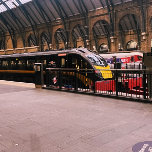 Inside a train station, a modern black train with yellow and red accents is parked at the platform, with another train visible in the background.