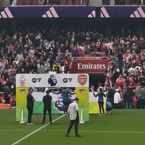 Soccer stadium filled with spectators, with officials and players on the field, and promotional banners on display.