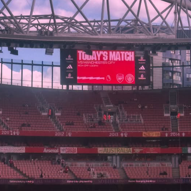 Large digital scoreboard displaying 'Today's Match VS Manchester City' at a stadium with pink sky in the background.