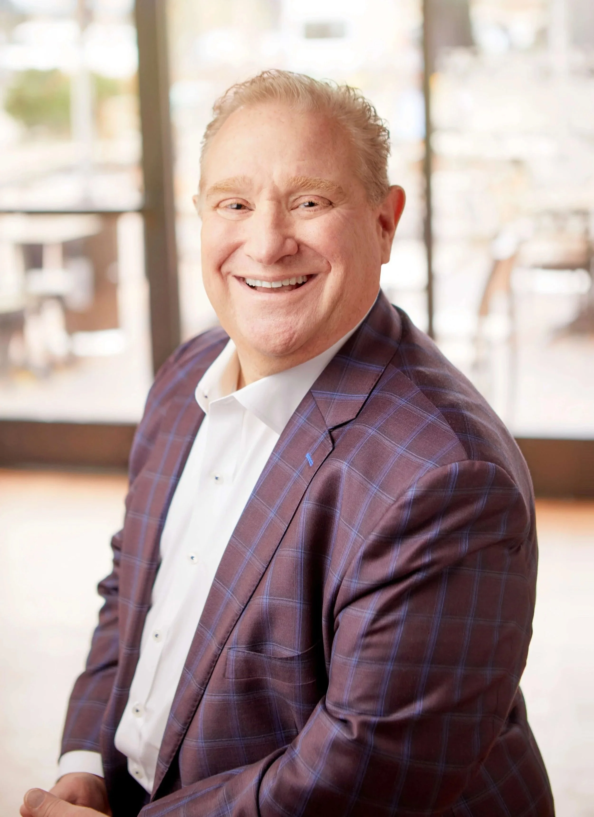 Chris Artinian in a suit jacket and white shirt sitting indoors during daytime.