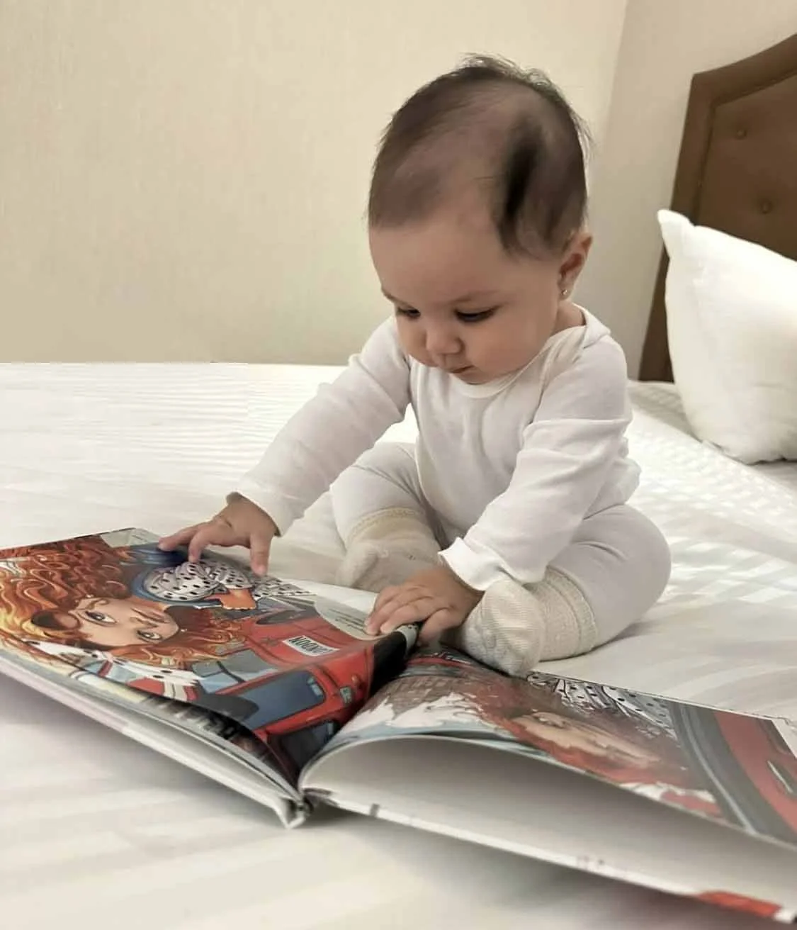 A young child in white pajamas sitting on a bed, looking at a colorful comic book