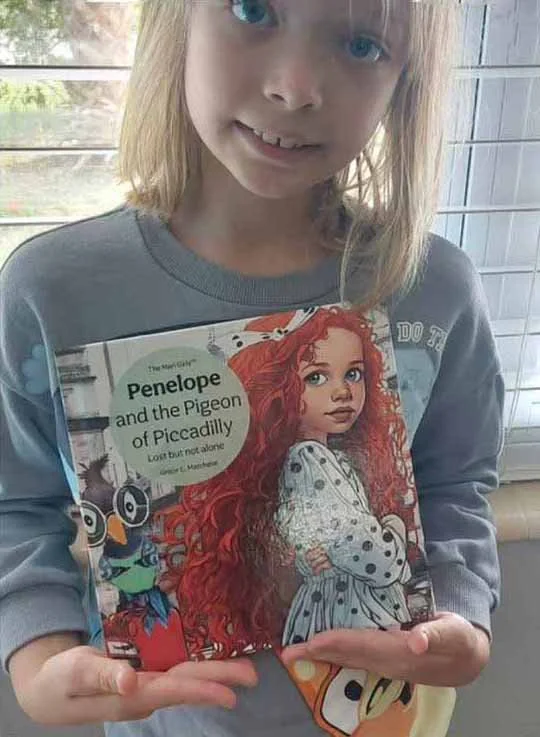 A young girl with blonde hair holding a book titled "Penelope and the Pigeon of Piccadilly" with an illustration of a girl with red curly hair on the cover.