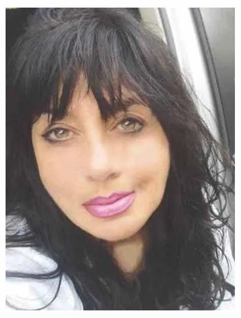 Close-up of a woman with dark, curly hair and pink lipstick, looking at the camera.